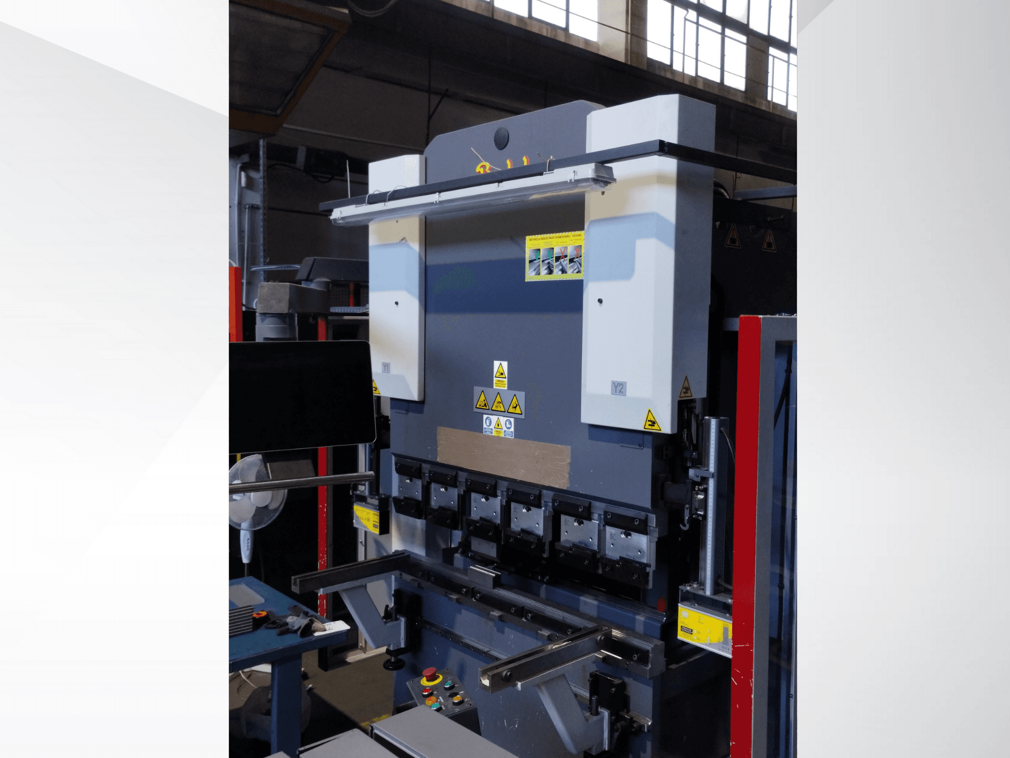 Máquina plegadora, vista frontal. Dispone de controles visibles, adhesivos de seguridad y múltiples portamatrices para un plegado de precisión.