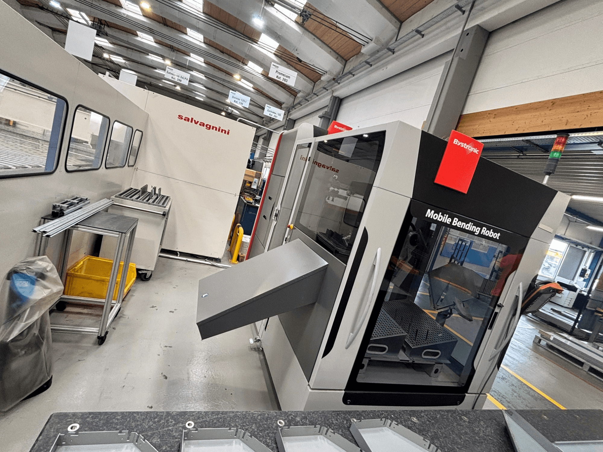 Plegadora Bystronic Xpert 40/1030, vista frontal en la que se aprecian el robot de plegado móvil y la zona de trabajo con piezas metálicas sobre una mesa.