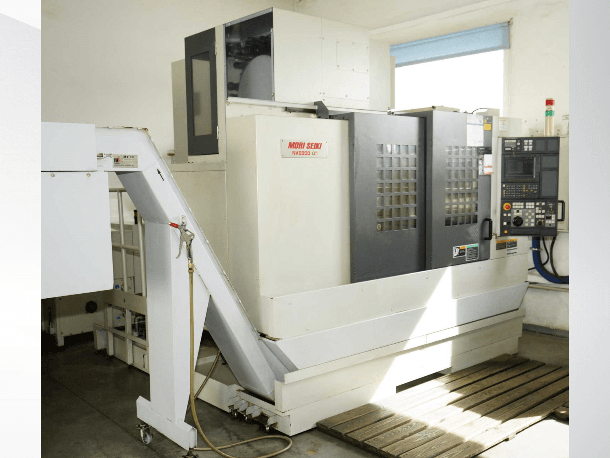 Centro de mecanizado vertical MORI SEIKI NV 5000 alpha1 en vista frontal, en el que se aprecian el panel de control, los dispositivos de seguridad y la zona de carga.