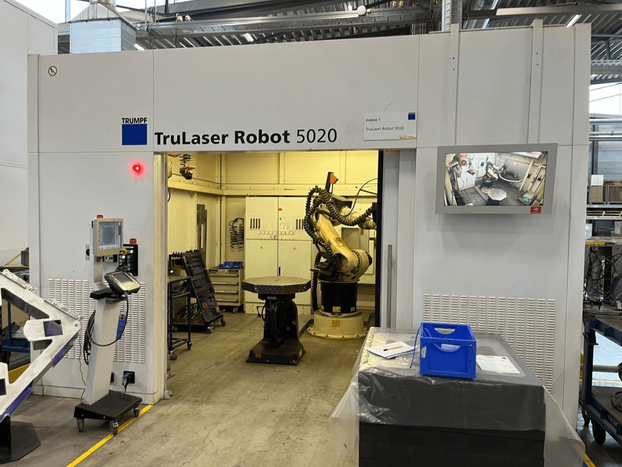 TRUMPF TruLaser Robot 5020 en un entorno industrial, con los mandos de control, un brazo robótico y una pantalla en la que se muestran las operaciones.