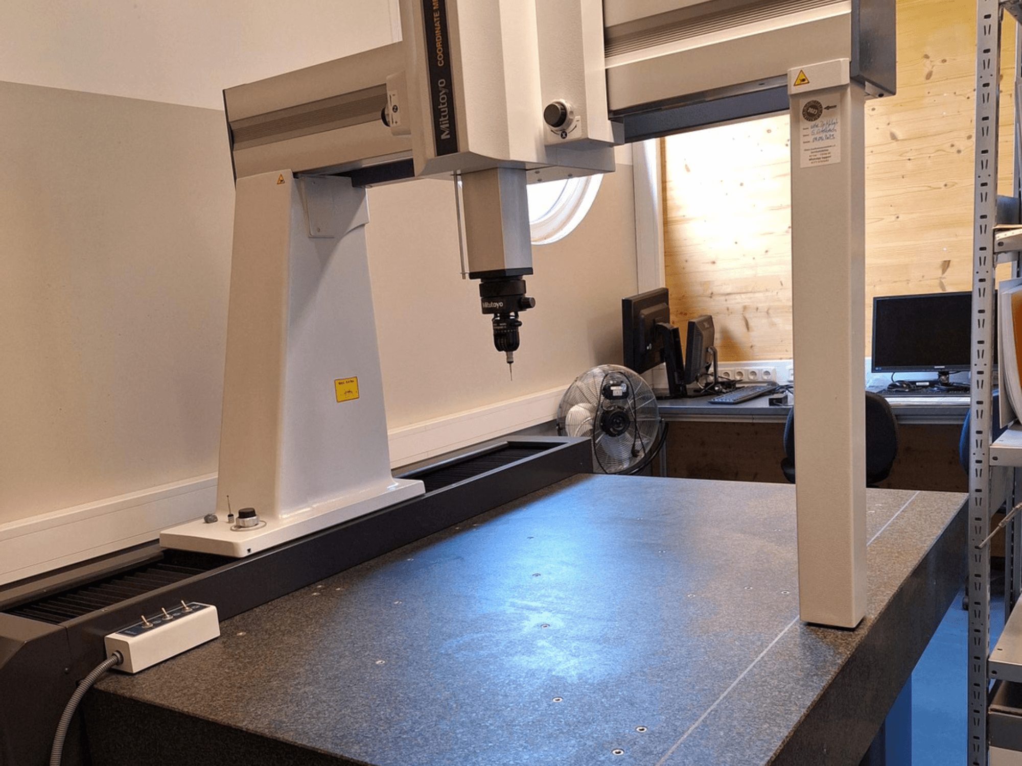 Robot de pórtico Mitutoyo Crysta-Plus M7106 en un taller, vista frontal, en la que se aprecian la sonda de medición y la placa de granito.