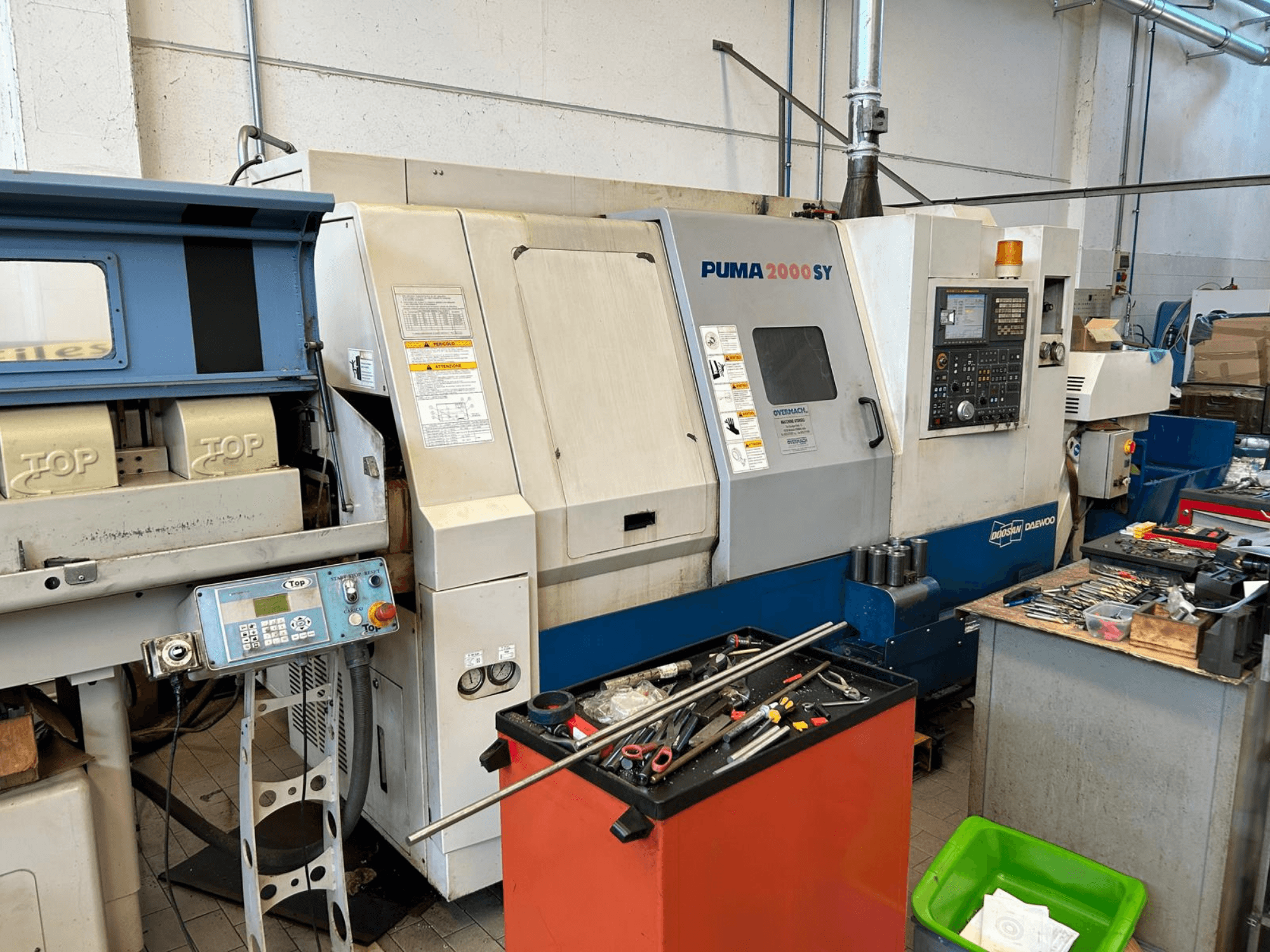 Torno horizontal DOOSAN PUMA 2000SY en un taller, vista lateral en la que se aprecian el panel de control y las herramientas situadas a su alrededor.