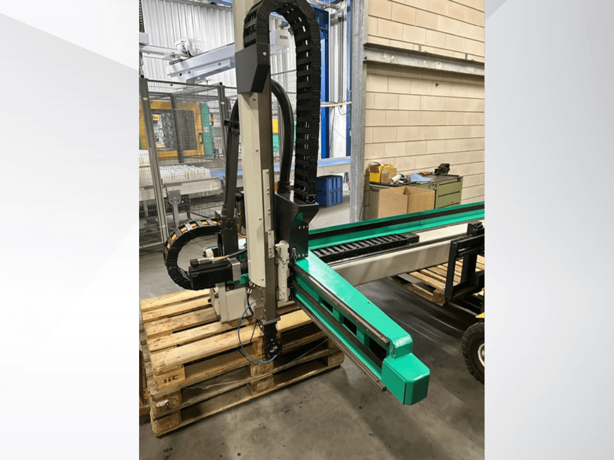Arburg Multilift Select 15kg quer, vista lateral del sistema de manipulación de piezas sobre palés de madera, mostrando el brazo robótico y los componentes de control.