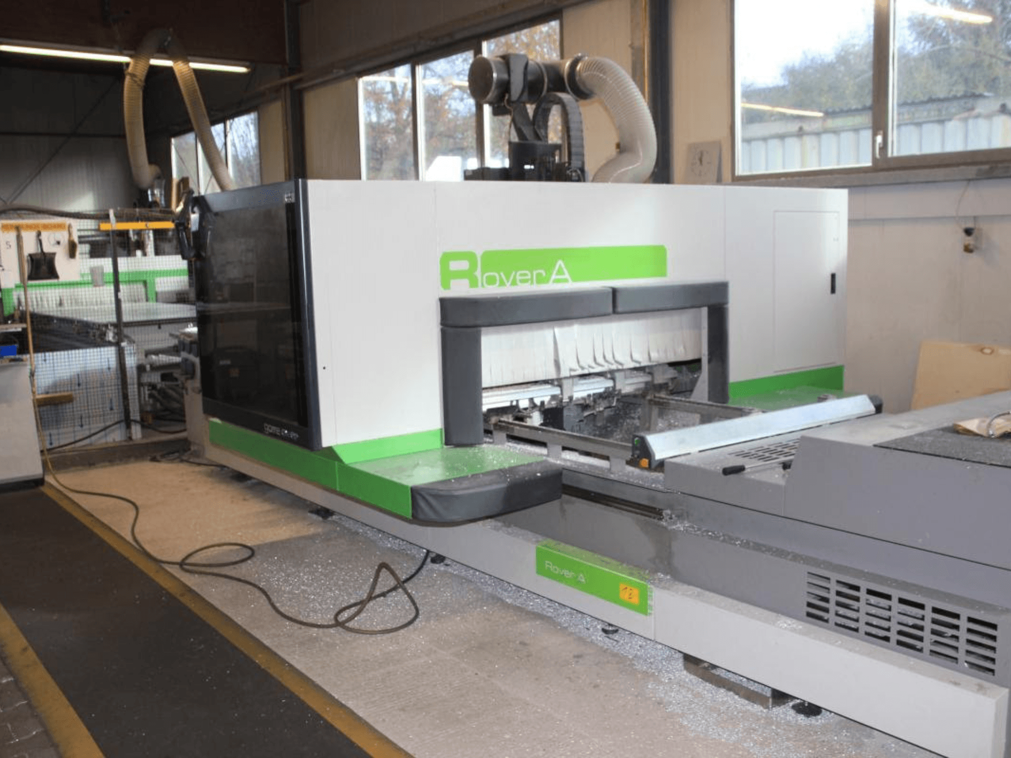 Fresadora CNC Rover A 1232 de BIESSE, vista lateral que muestra la zona de corte y el panel de control en un entorno industrial.