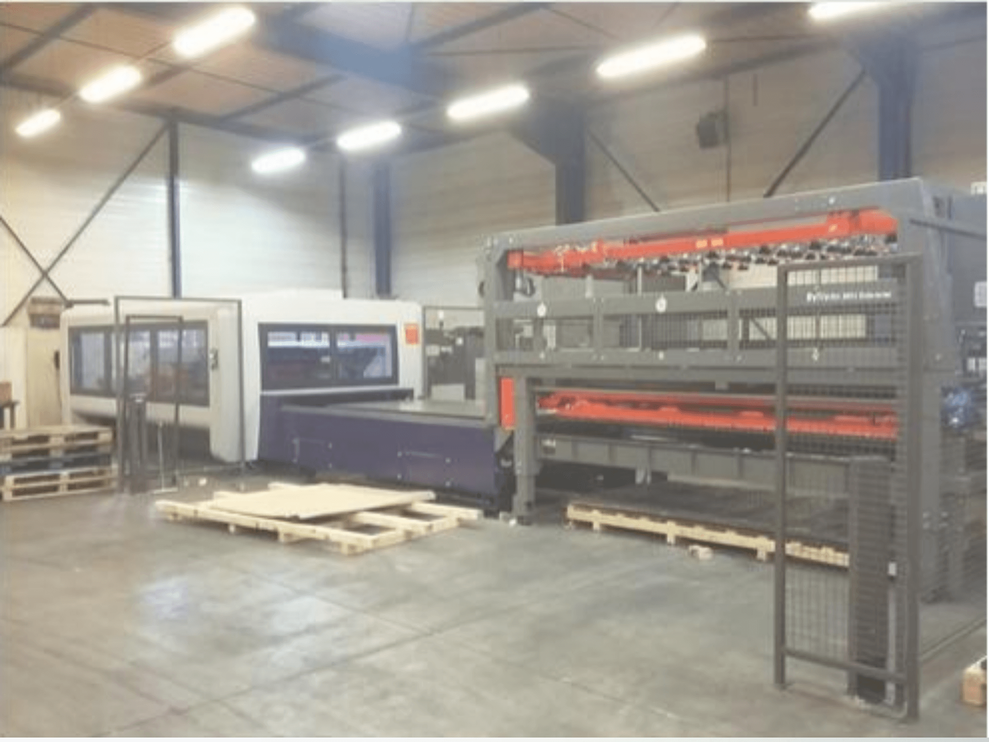 Instalación de maquinaria industrial en un almacén; incluye una cortadora láser gris y una fresadora CNC morada, vista frontal con palés.