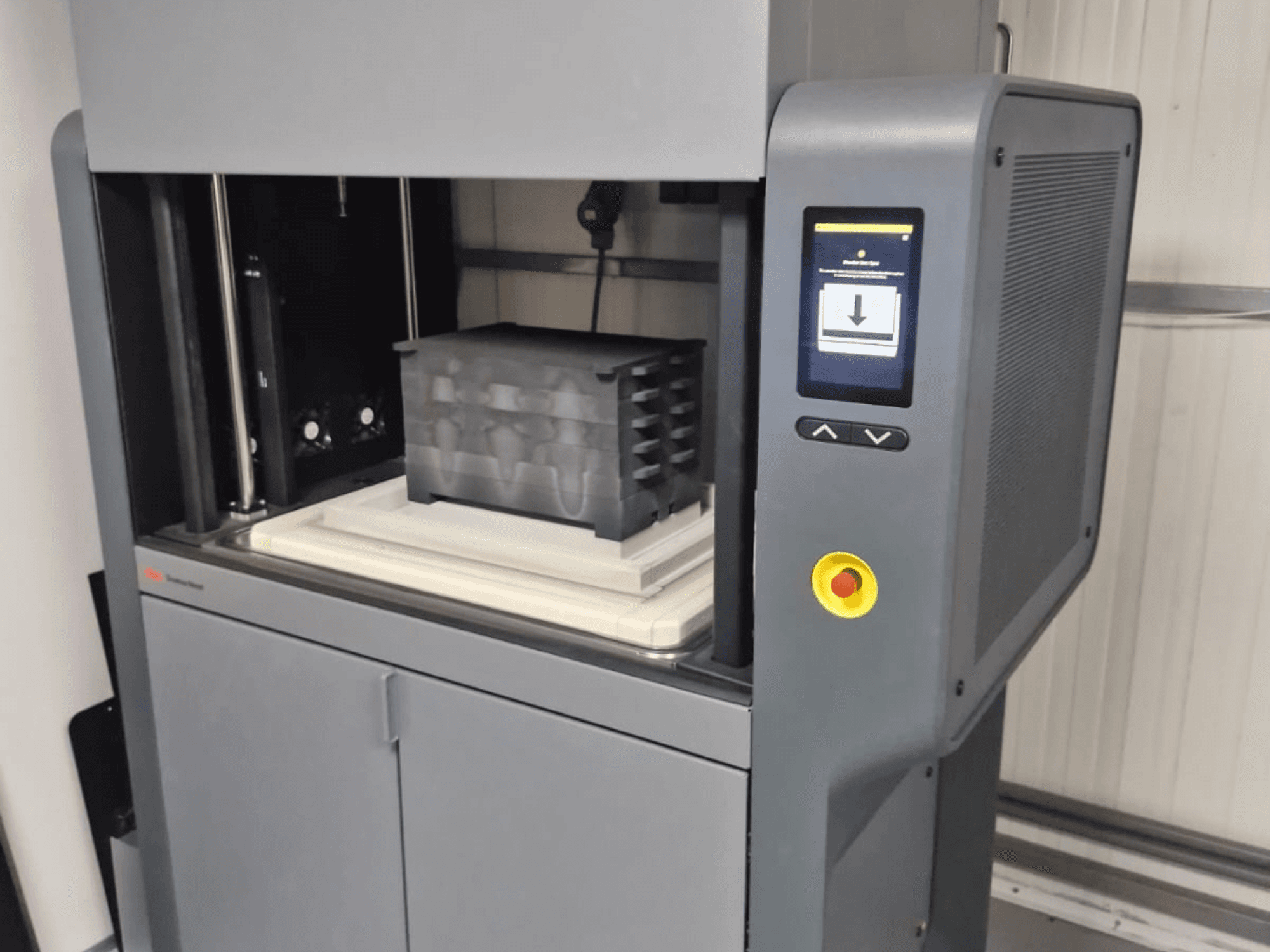 Impresora 3D Metal Studio 2 de Desktop Metal, vista frontal que muestra el panel de control y el lecho de impresión con un contenedor negro.