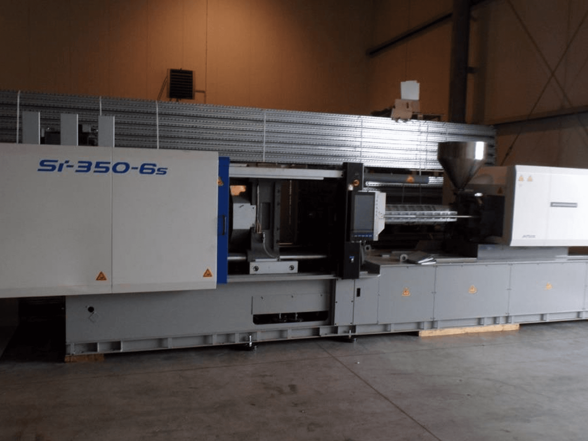 Máquina de moldeo por inyección Si-350-6s en vista lateral, con tolva y panel de control, situada en un amplio entorno industrial.