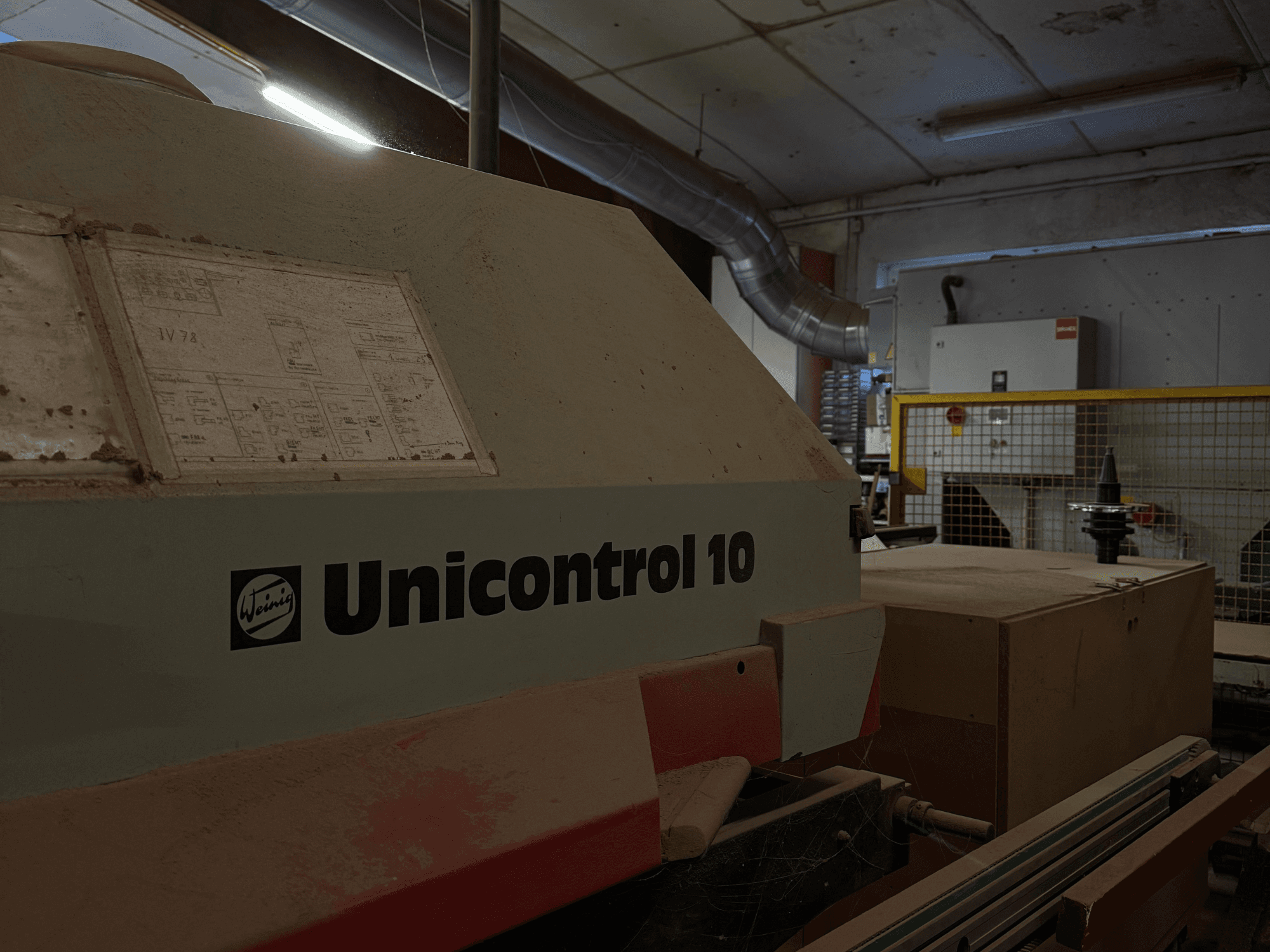 Máquina Weinig Unicontrol 10 vista desde un ángulo lateral, superficie polvorienta, esquemas técnicos visibles en el panel frontal.