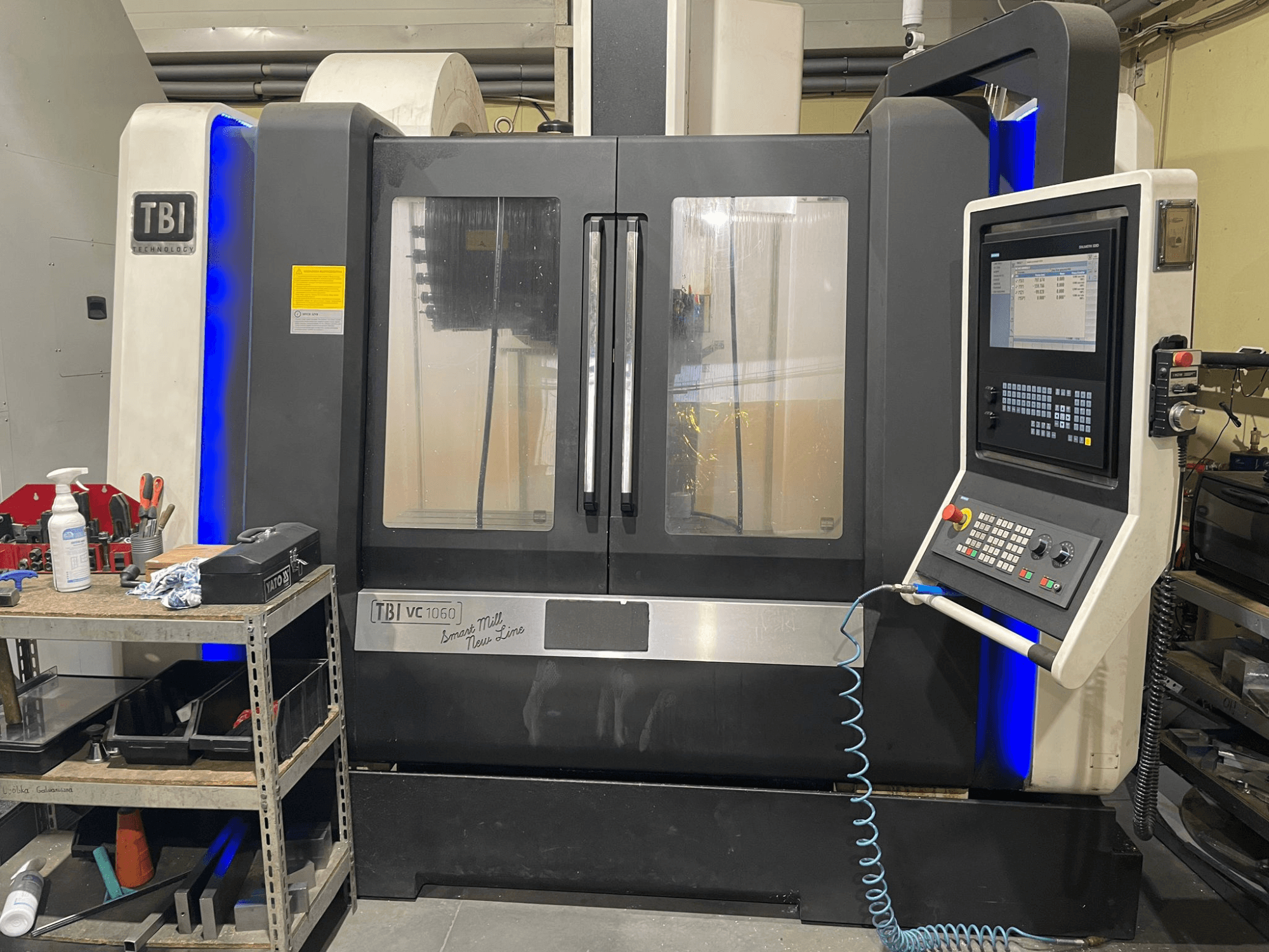 Centro de mecanizado vertical TBI VC 1060 HH, vista frontal, mostrando el panel de control, la cubierta antipolvo y los detalles azules iluminados.