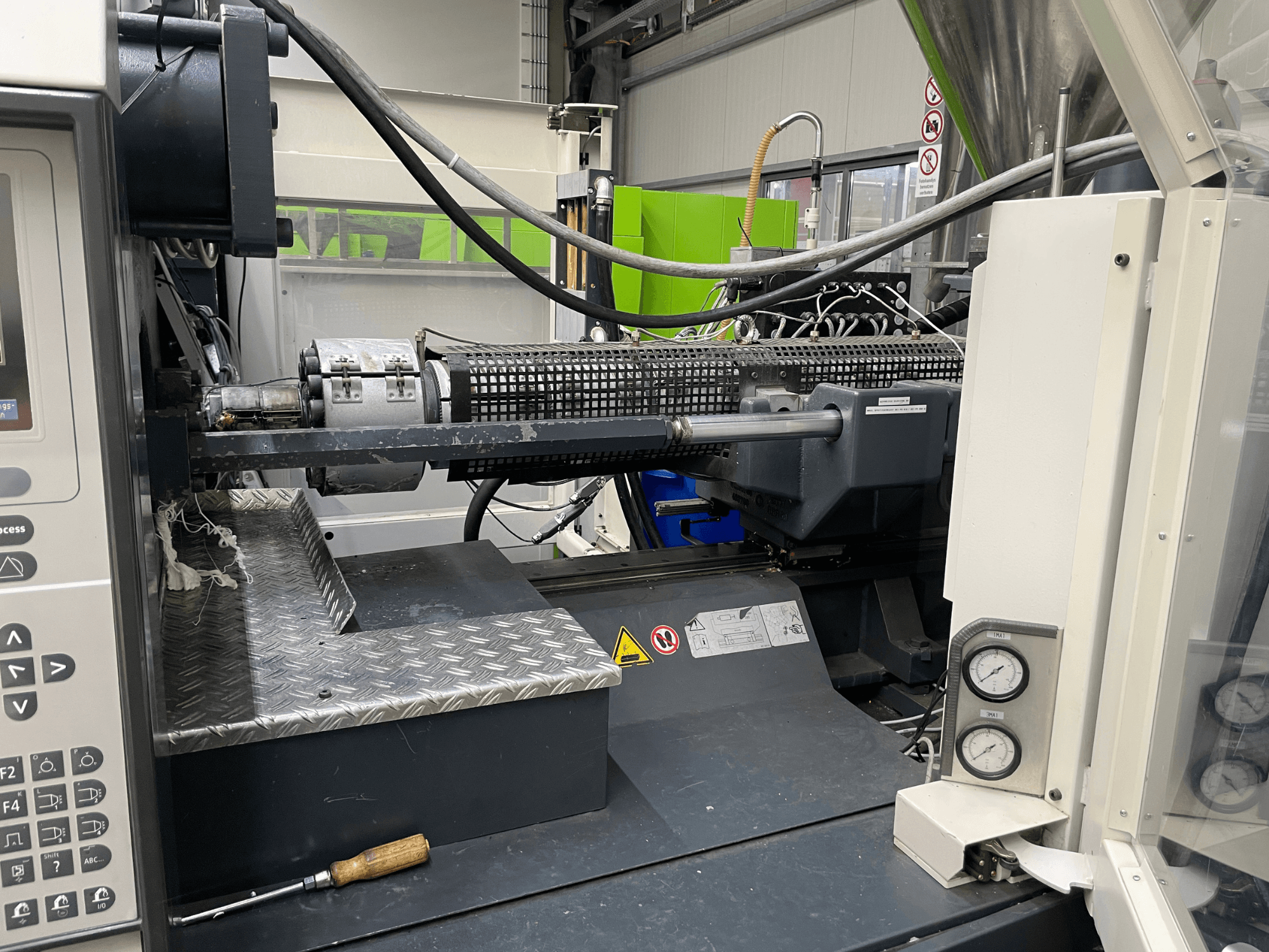 Vista lateral de máquina de moldeo por inyección con panel de control, extrusora y manómetros visibles, ideal para tareas de fabricación.