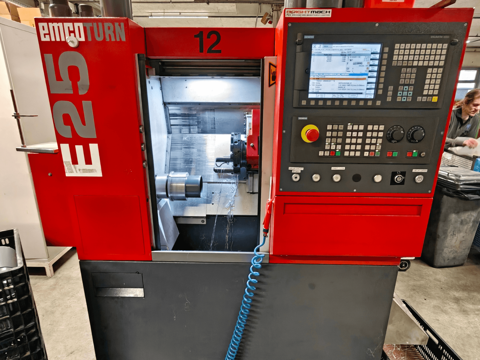 Vista frontal de la máquina EMCO TURN E25, con el panel de control, el portaherramientas y la zona interior con la herramienta de corte visible.