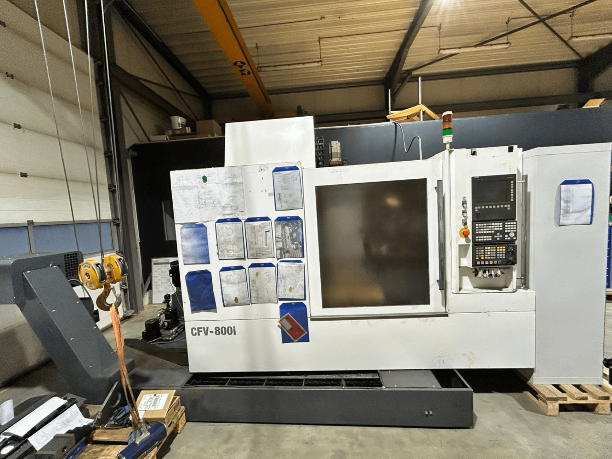 Máquina CNC CFV-800i mostrada en vista frontal, con panel de control, documentos en el lateral y puente grúa en configuración de fábrica.