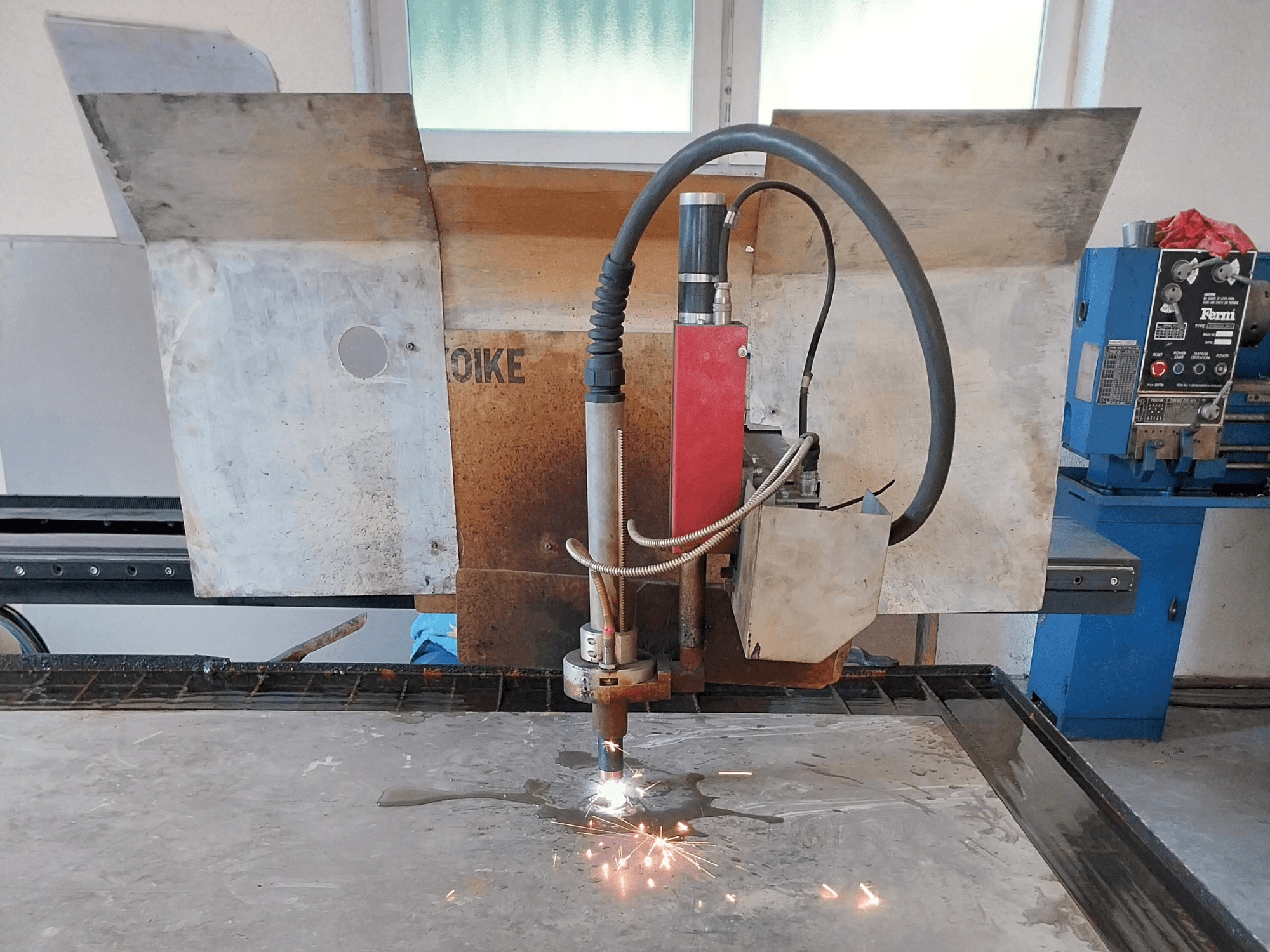 Vista frontal de una cortadora de plasma Oike con chispas saltando, colocada sobre una superficie metálica en una mesa de trabajo.