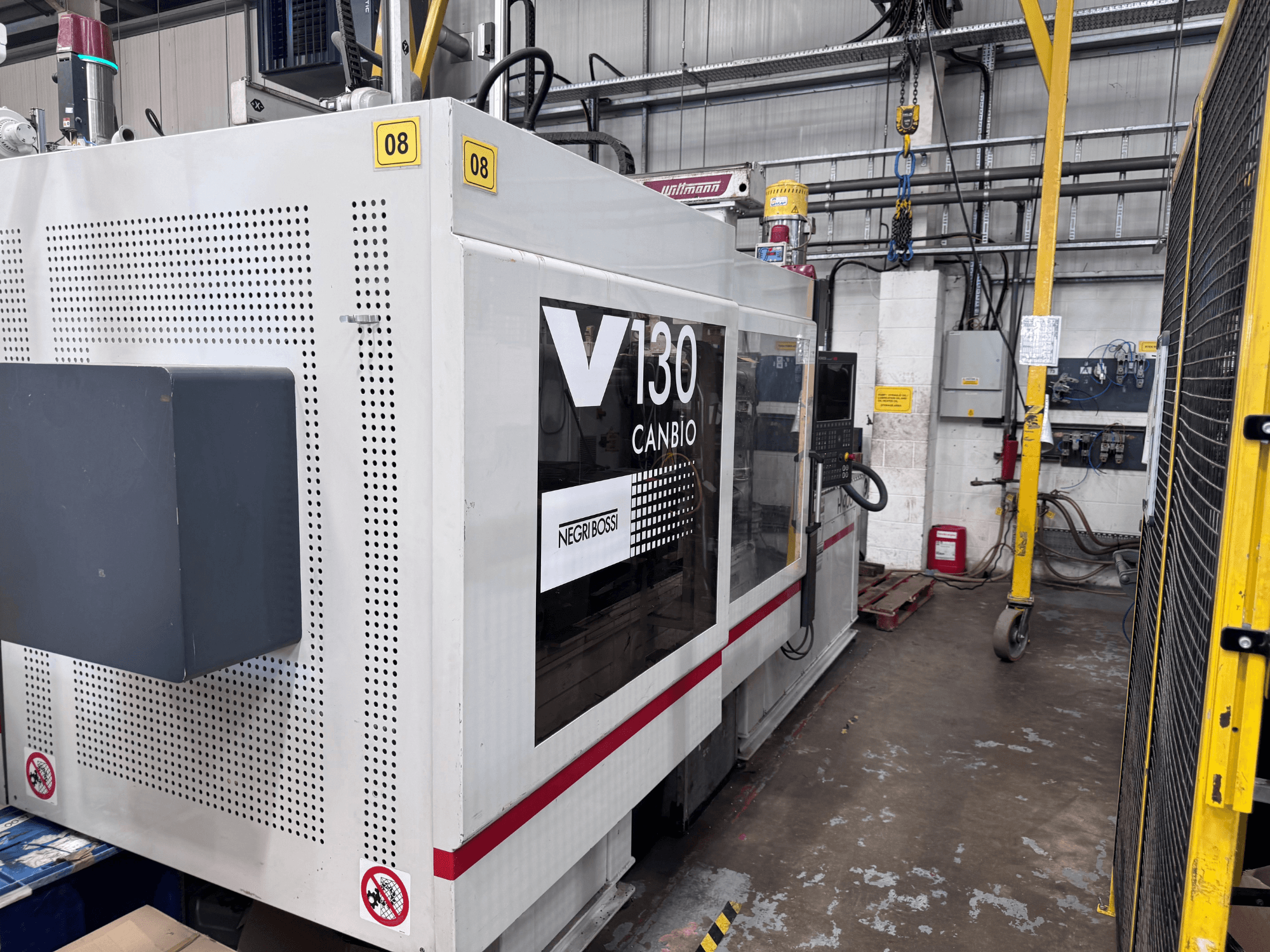 Máquina de moldeo por inyección hidráulica Negri Bossi 1300H-400, vista lateral, en la que se aprecian el panel de control y la señalización de seguridad.