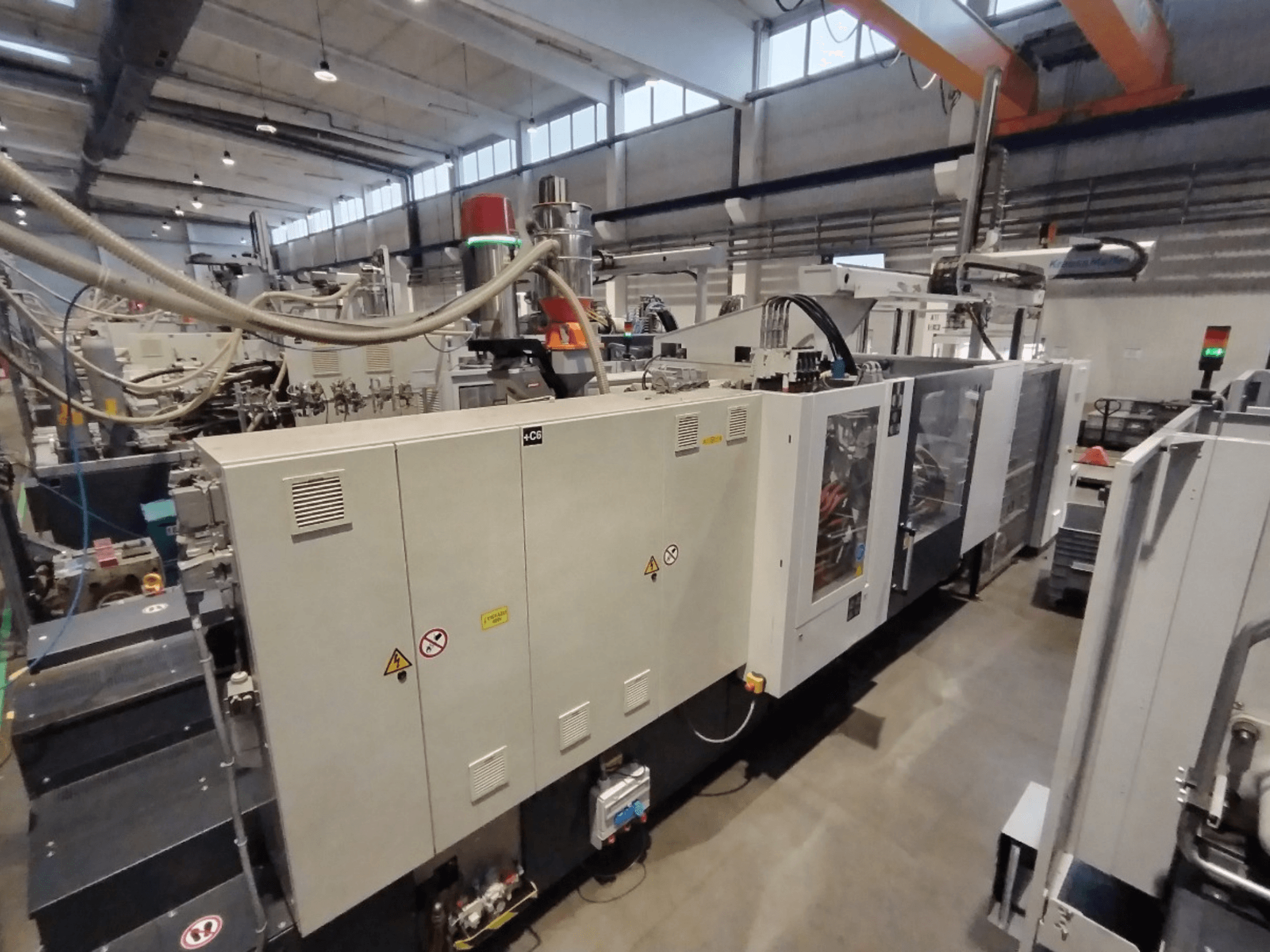 Máquina industrial de moldeo por inyección mostrada desde una vista lateral, con panel de control y advertencias de seguridad. Marca: Desconocida.