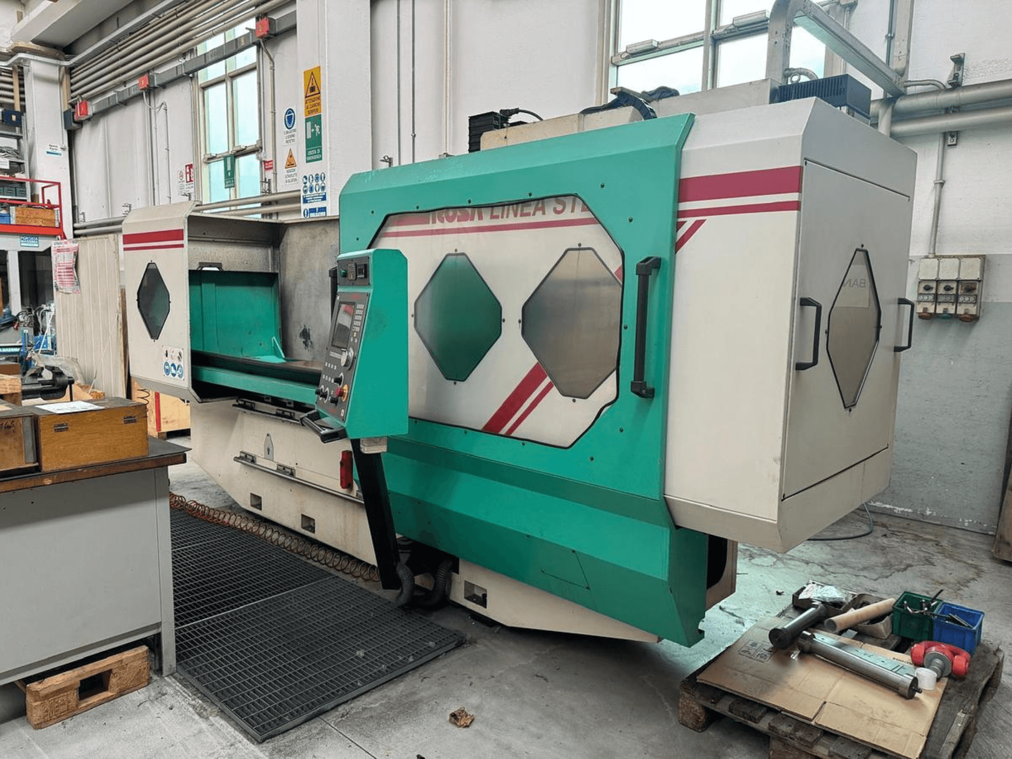 Máquina de precisión verde y blanca, vista frontal, con panel de control, área de trabajo y herramientas sobre un palé. Marca: BAMB.