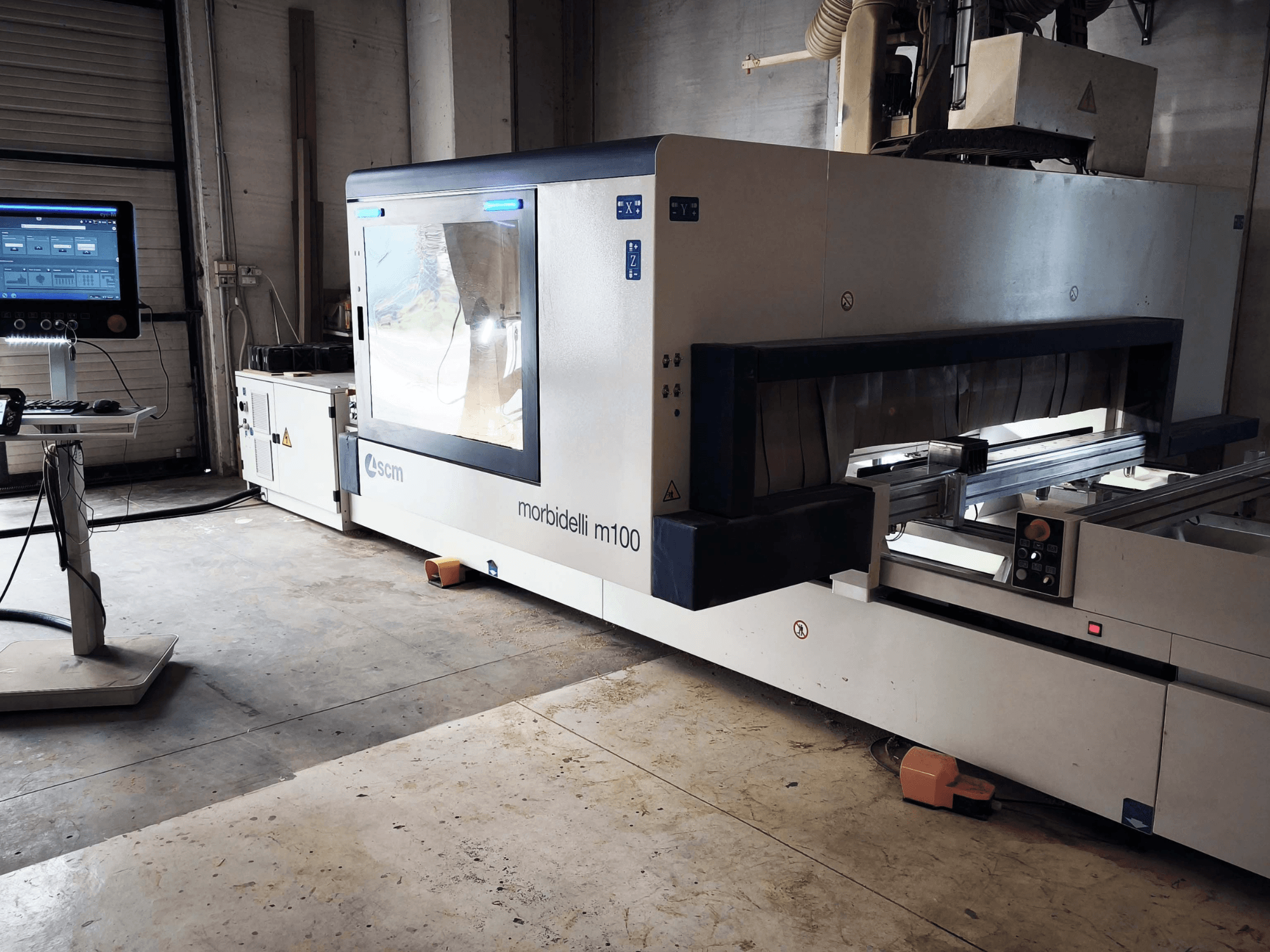 Centro de mecanizado de madera CNC SCM Morbidelli M 100 en vista lateral, en el que se aprecian el panel de control, la zona de trabajo y los elementos de seguridad.
