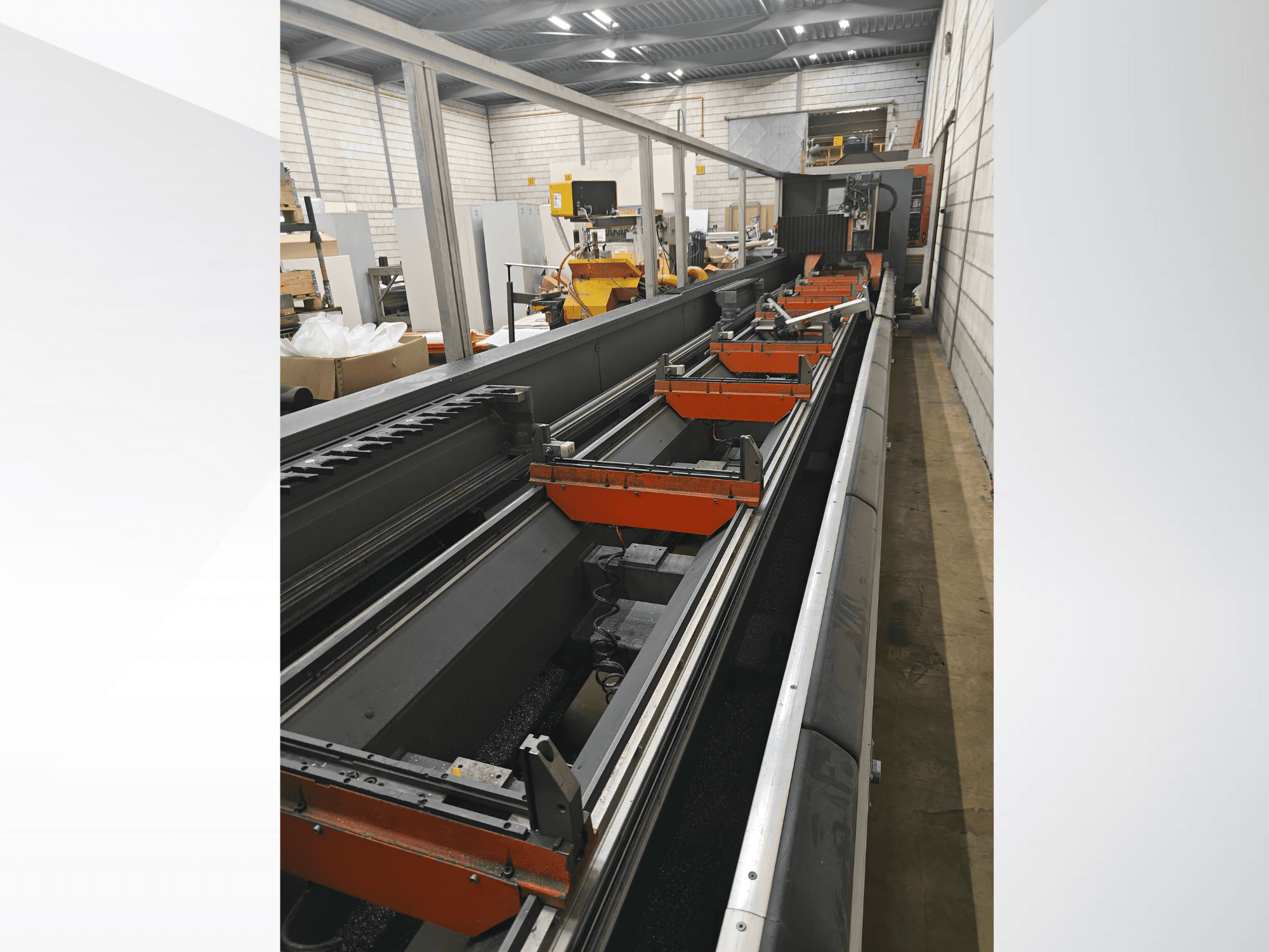 Vista lateral de máquina CNC industrial, con guías lineales, pinzas naranjas y componentes de precisión en un entorno de almacén.