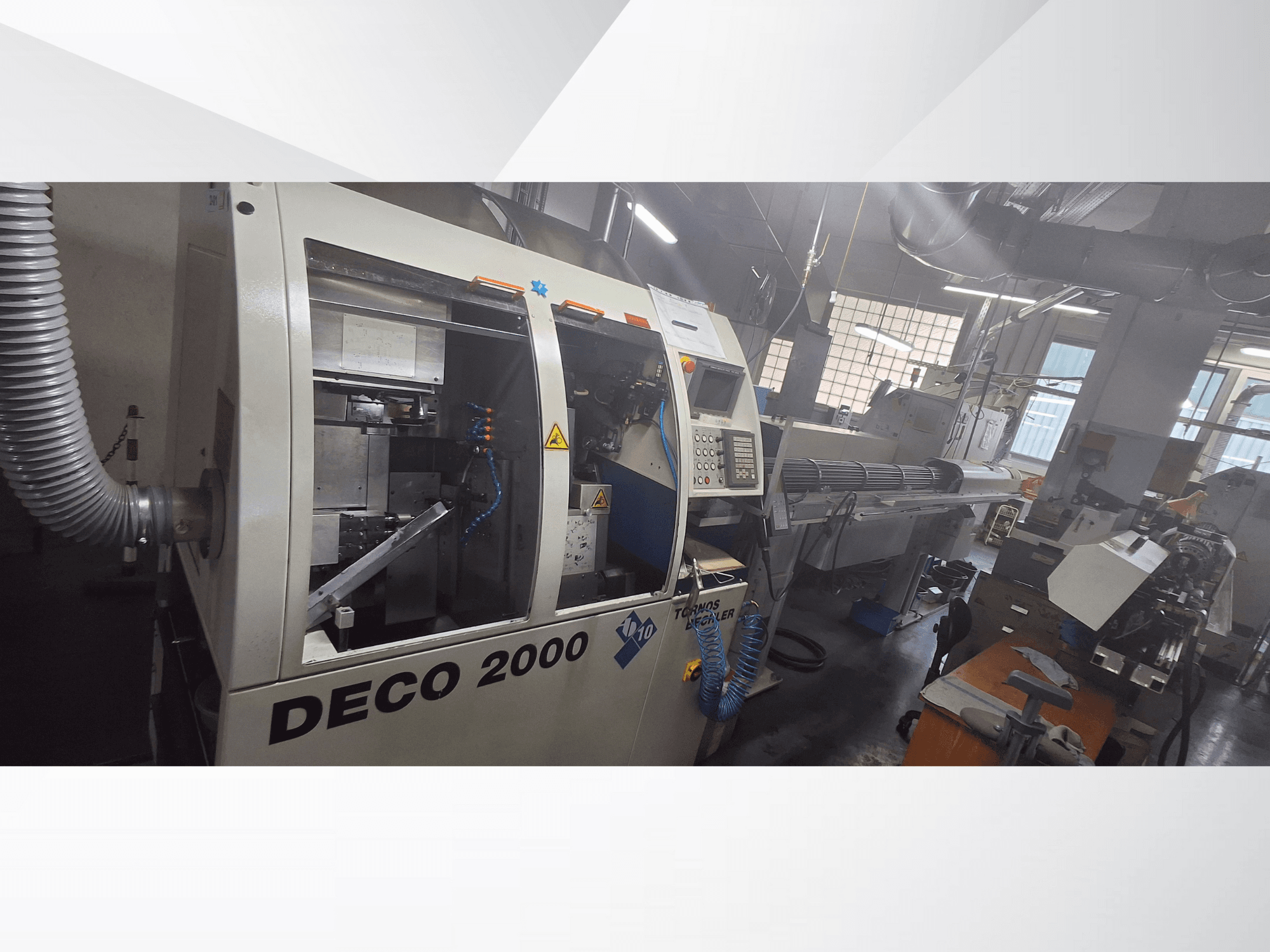 Máquina CNC DECO 2000 en un taller, vista frontal, mostrando los controles y una configuración de pieza larga a la derecha.