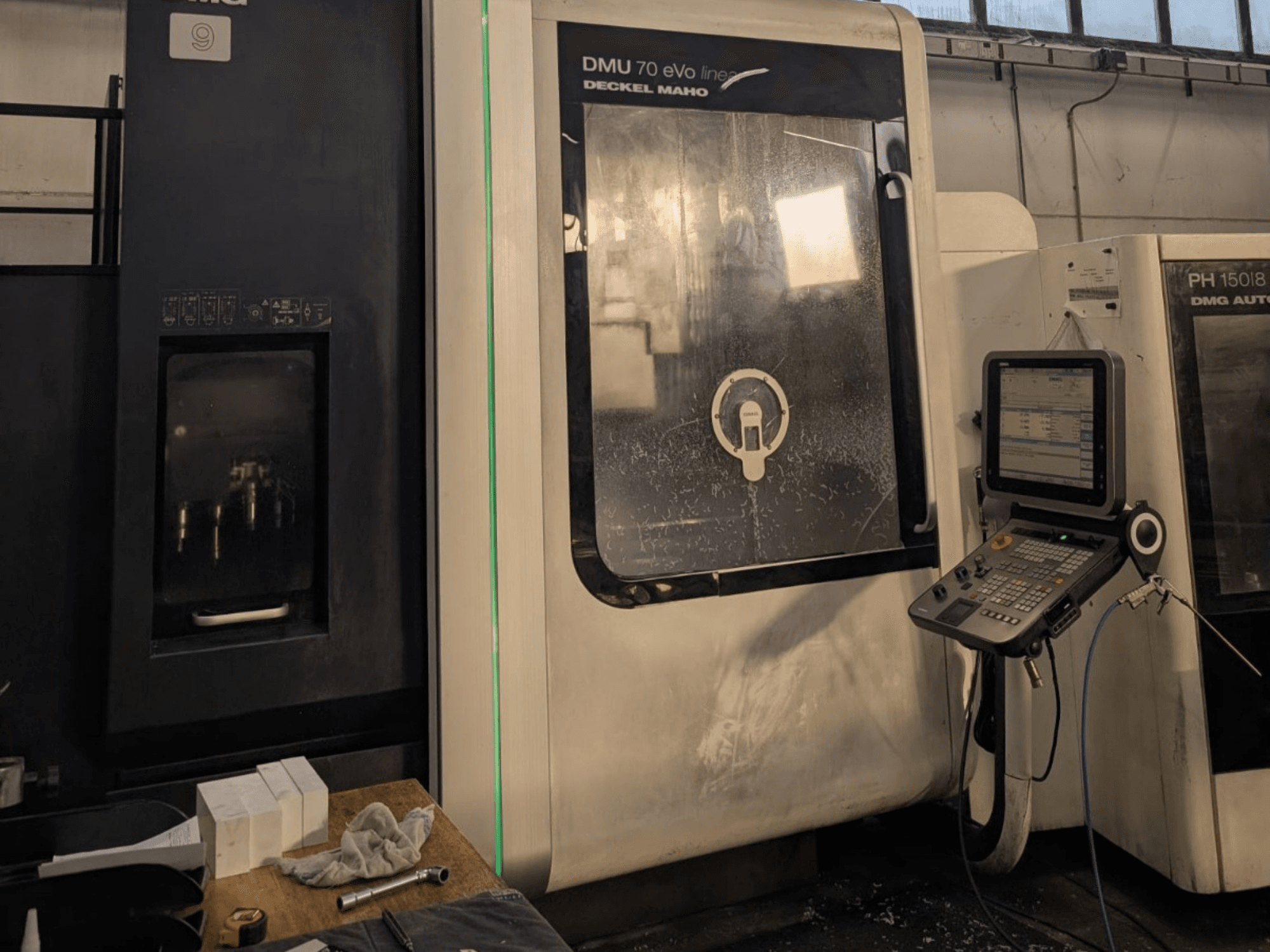 Centro de mecanizado vertical DMG DECKEL MAHO DMU 70 EVO Linear, vista frontal con panel de control, herramientas y espacio de trabajo visibles.