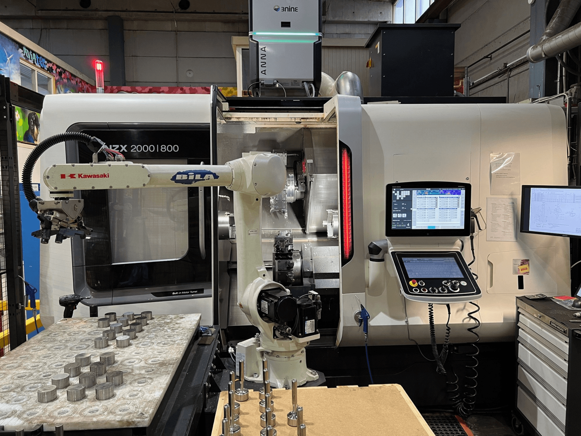 Torno horizontal DMG MORI NZX 2000/800SY en un taller, en el que se aprecian el brazo robótico de Kawasaki y los mandos de control.