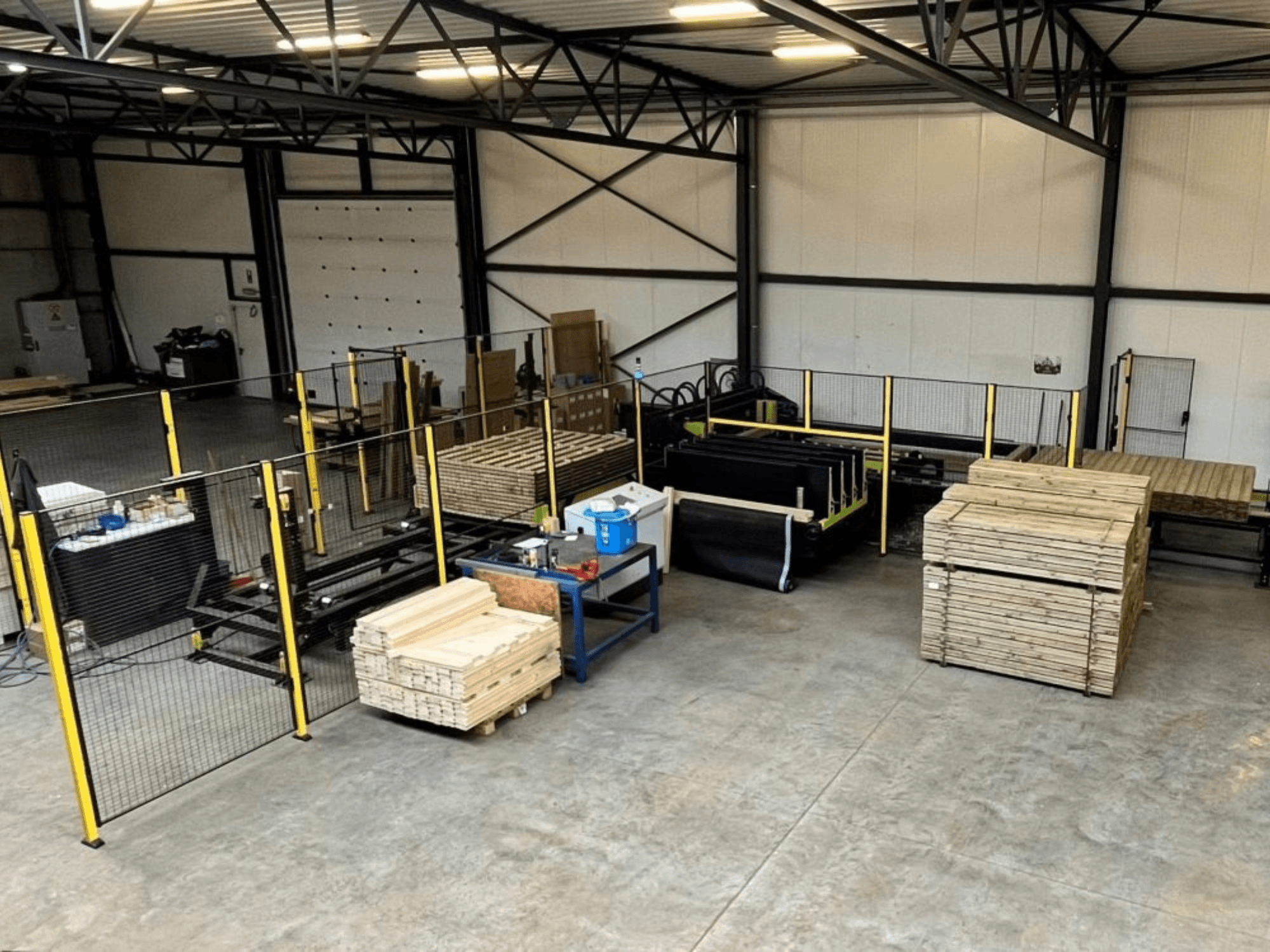 Línea de producción completa (ISM ATM-01) para madera, vista desde arriba, mostrando maquinaria, palés de madera y vallas de seguridad.