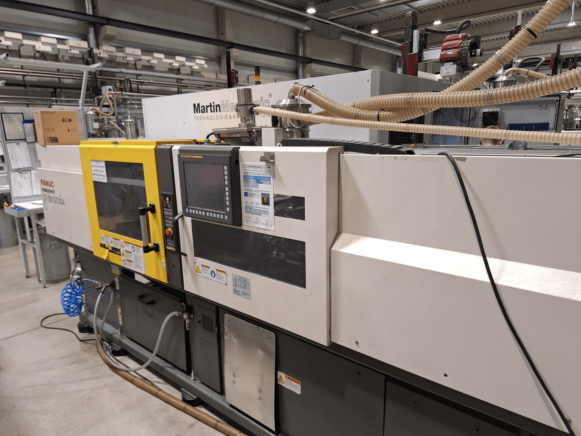 Máquina de moldeo por inyección eléctrica FANUC Roboshot S100iA, vista lateral, equipada con pantalla táctil y etiquetas de seguridad.