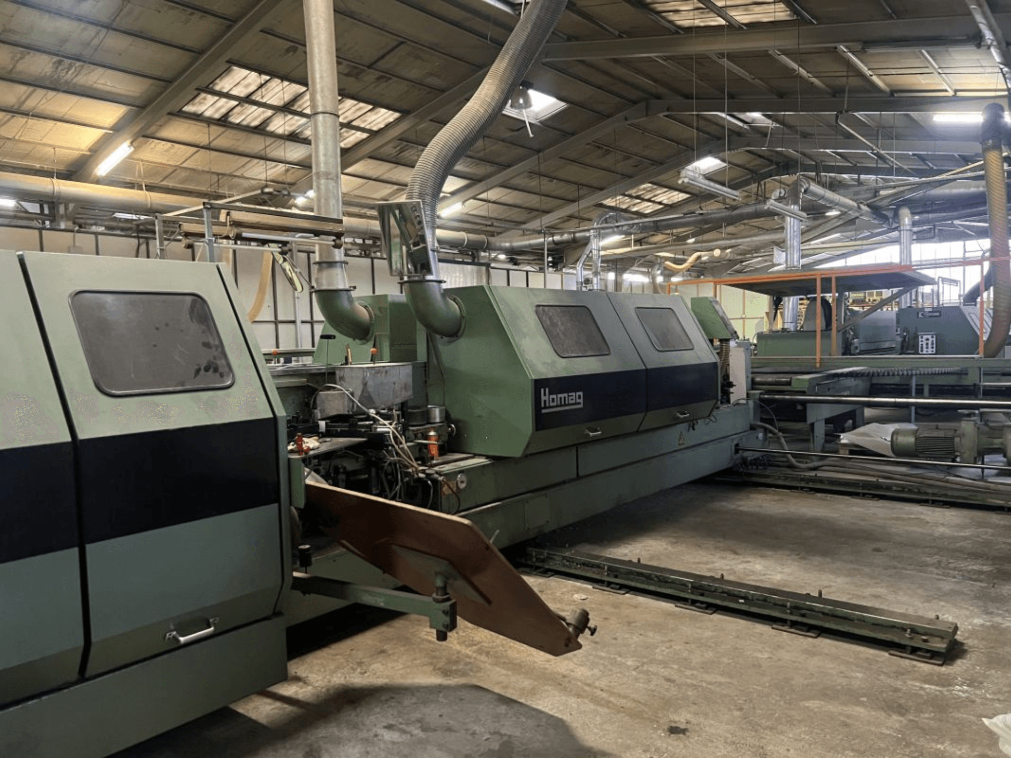 Máquina industrial Homag en verde, vista lateral, con componentes operativos y panel de control visibles en un entorno de almacén.