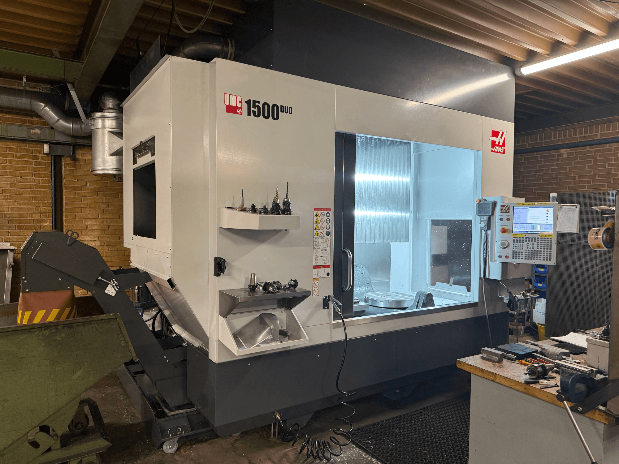Máquina CNC Haas UMC 1500DUO, vista frontal, cuenta con una gran ventana, panel de control y portaherramientas en un estante.
