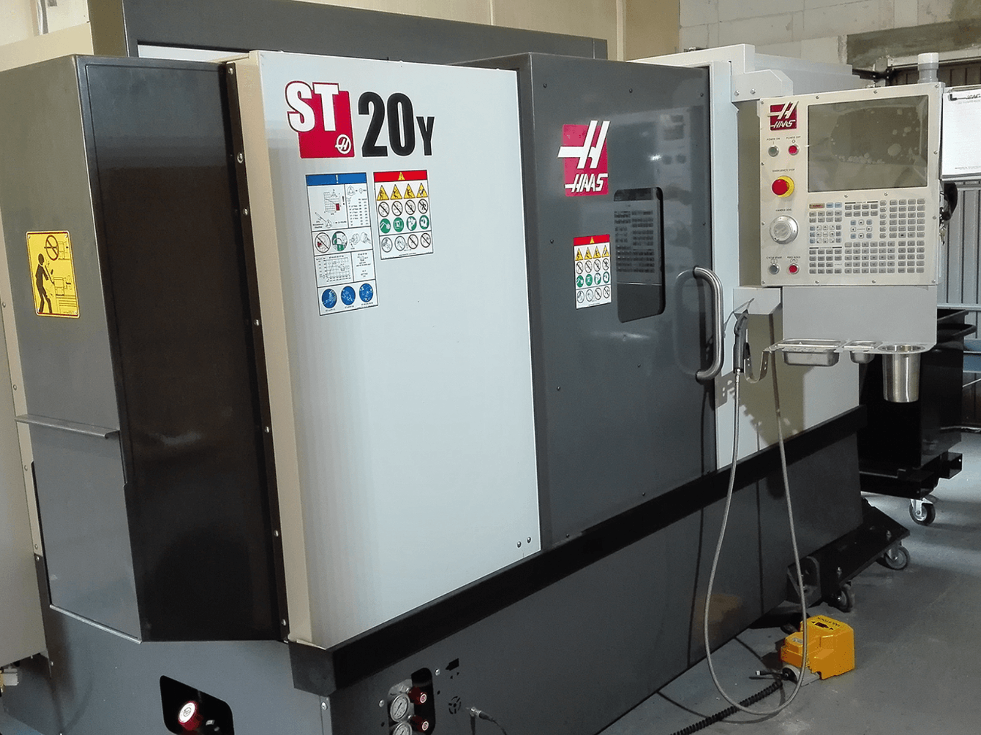 Torno CNC Haas ST20Y en vista frontal, con panel de control, etiquetas de seguridad y sistema de refrigeración.