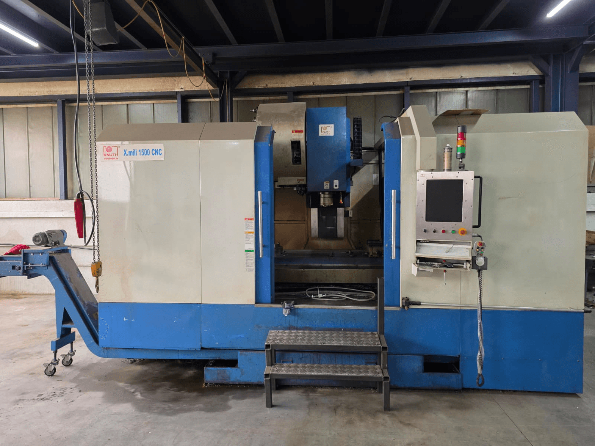 Centro de mecanizado vertical CNC KNUTH X-MILL 1500, vista lateral, en la que se aprecian el panel de control, los escalones y la cinta transportadora de salida.