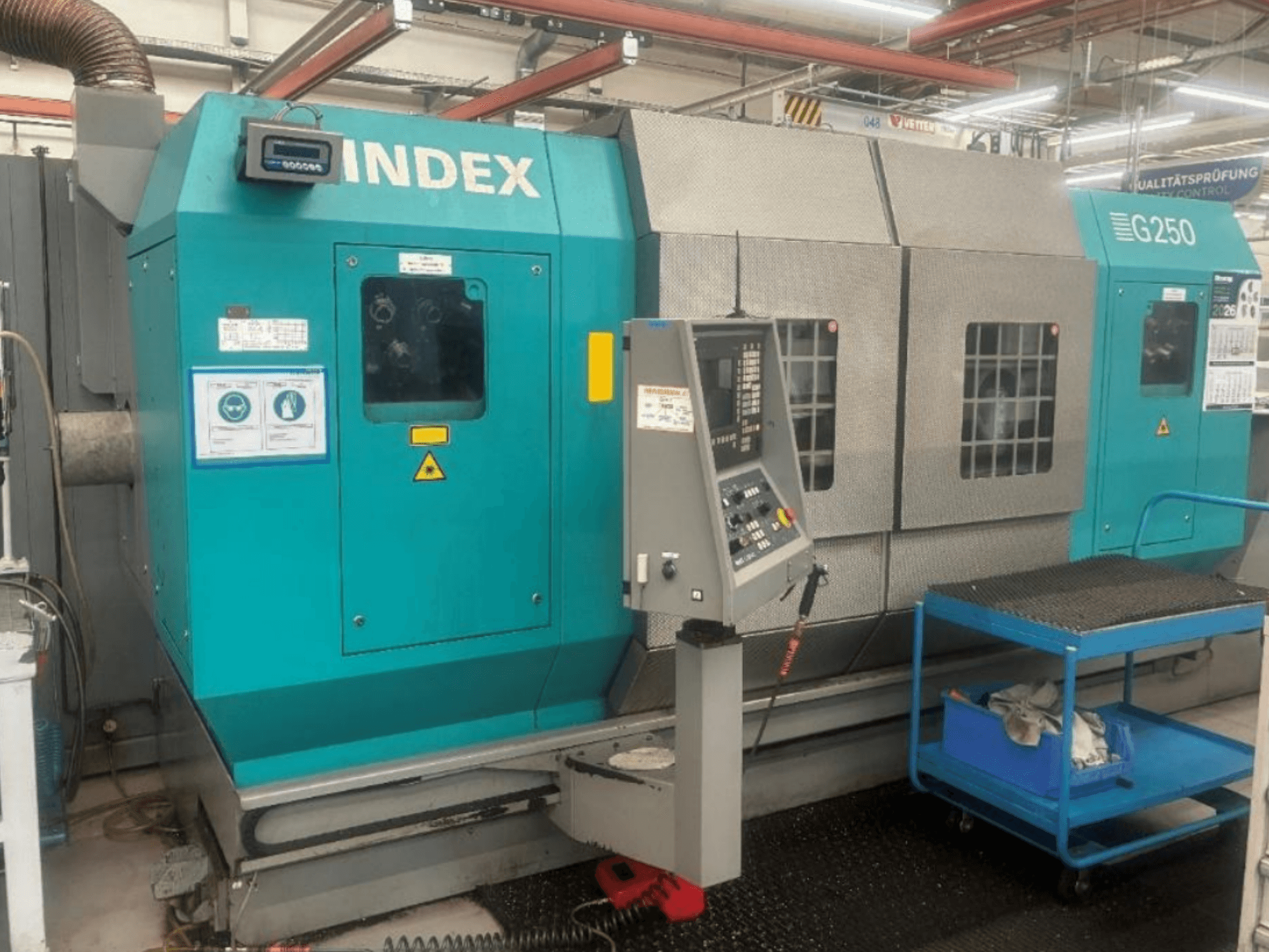 Torno horizontal INDEX G250, vista frontal en la que se aprecian el panel de control y la carcasa metálica, con etiquetas de seguridad y un carro azul.