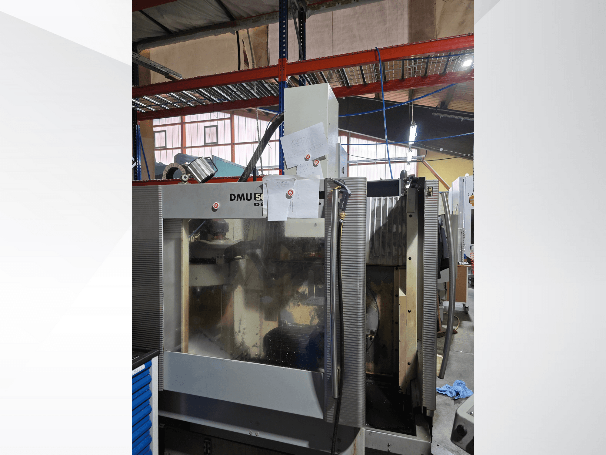 Centro de mecanizado CNC de 3 ejes DMU 50 en un taller, mostrado de frente, mostrando componentes operativos y documentos adjuntos.