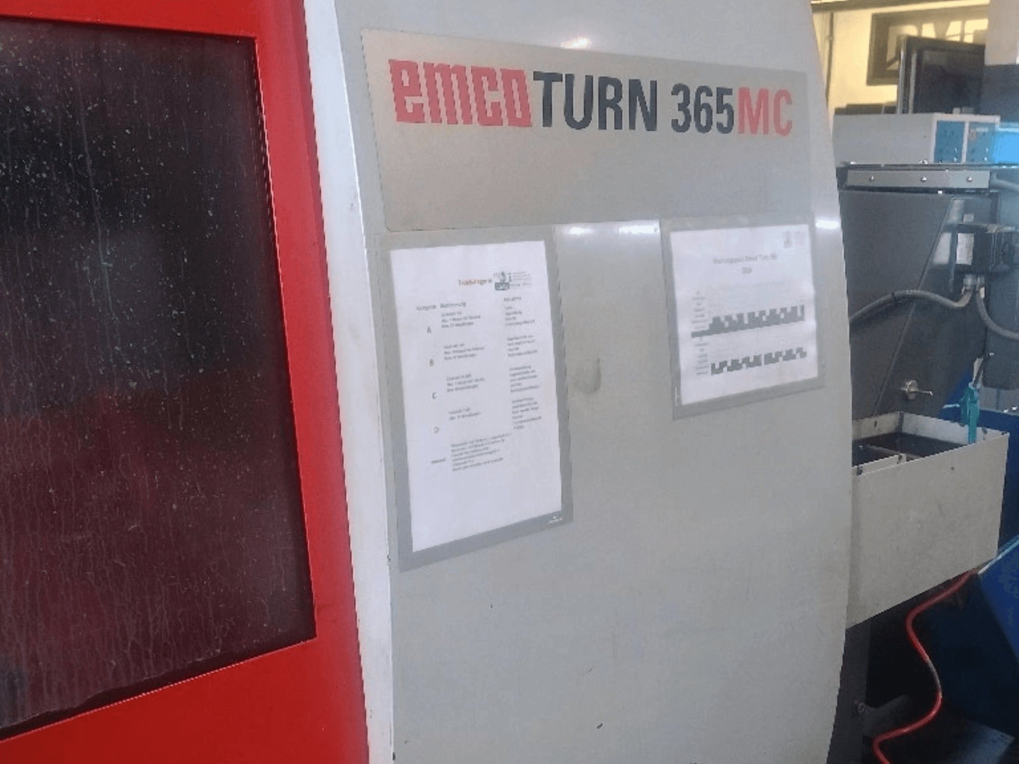 Torno horizontal EMCO EmcoTurn 365 MC, vista lateral en la que se aprecian el panel de control, los manuales y el depósito azul de líquido refrigerante.