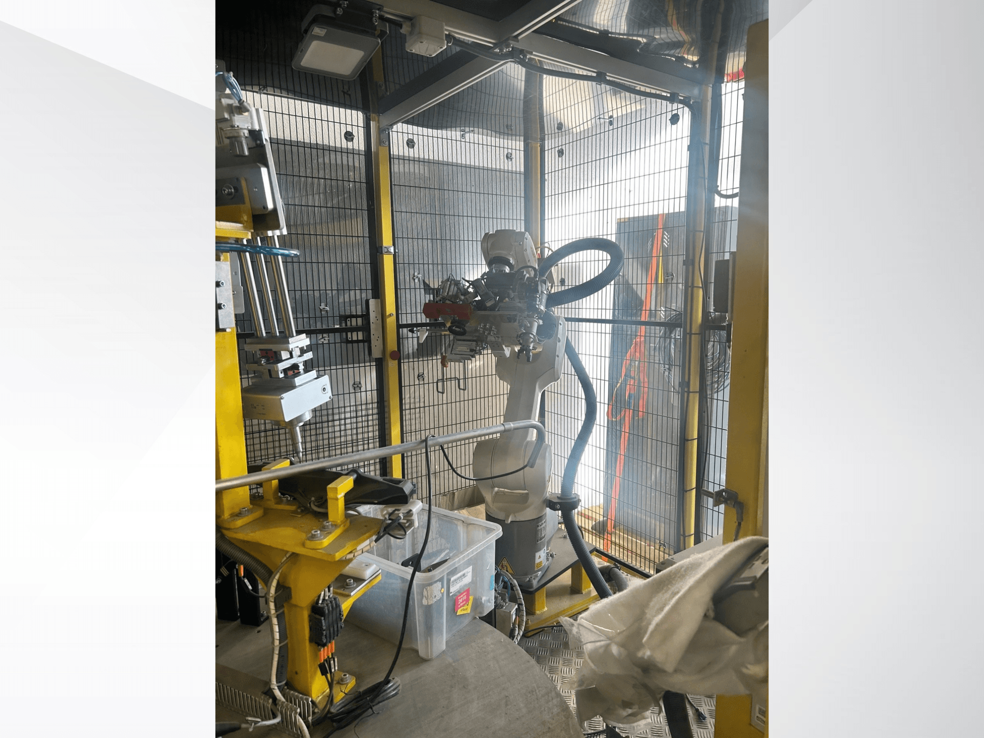 Brazo robótico del sistema de automatización automovilística MEI dentro de una cabina de seguridad, vista frontal, en la que se aprecian los componentes mecánicos y los controles.