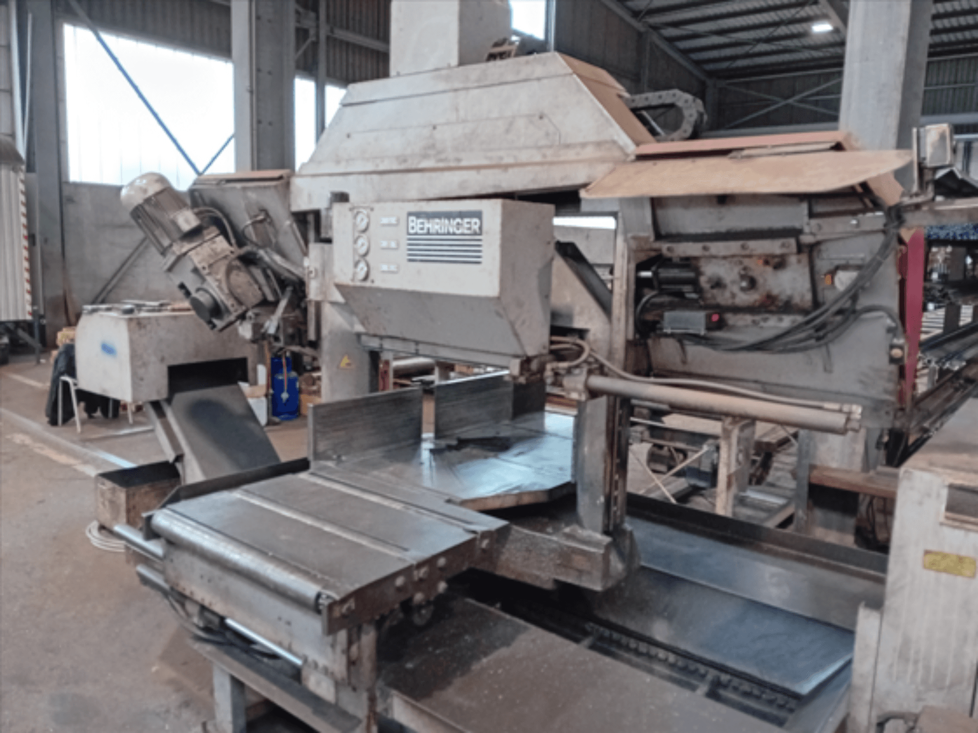 Sierra de cinta Behringer, vista frontal, cuenta con una gran hoja, motor y mesa ajustable, ideal para el corte de metal en un taller.