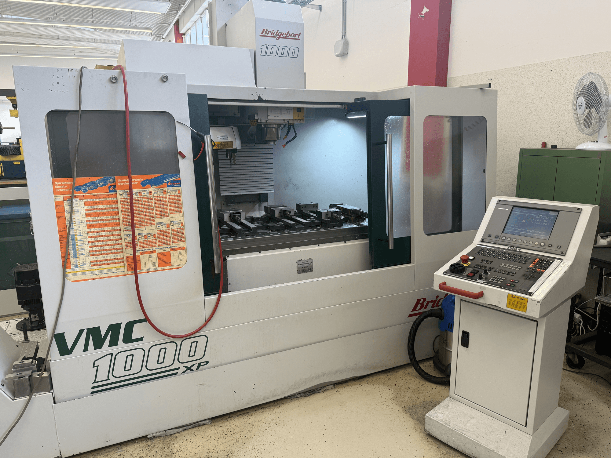 Vista frontal del centro de mecanizado vertical Bridgeport VMC 1000 XP, en la que se aprecian los controles, el área de trabajo y los soportes para herramientas.