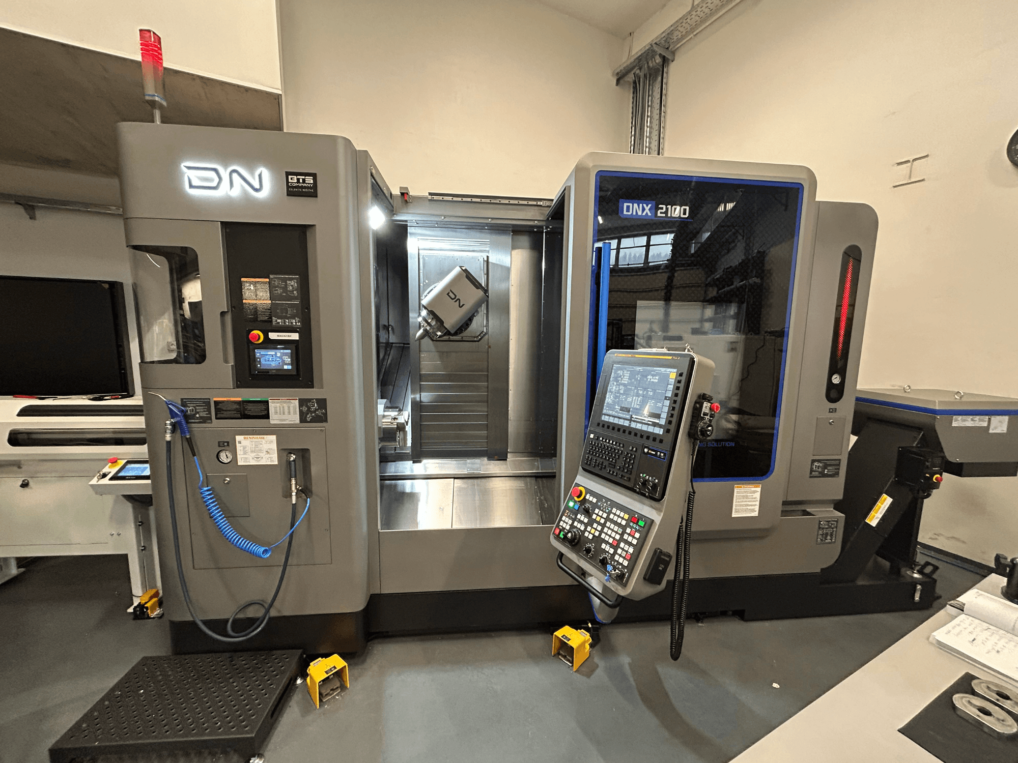 Máquina CNC DN ONX 2100, vista frontal, presenta panel de control, área de trabajo y herramienta. Equipada con luz de seguridad e indicadores de funcionamiento.