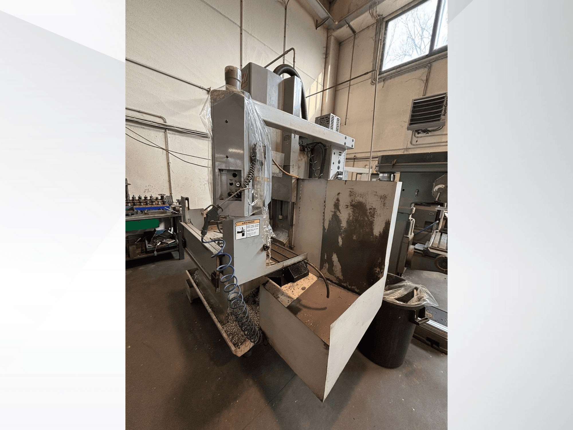 Fresadora vertical con cubierta protectora, vista lateral; incluye manguera de refrigerante y panel de control visible. Ideal para mecanizado.