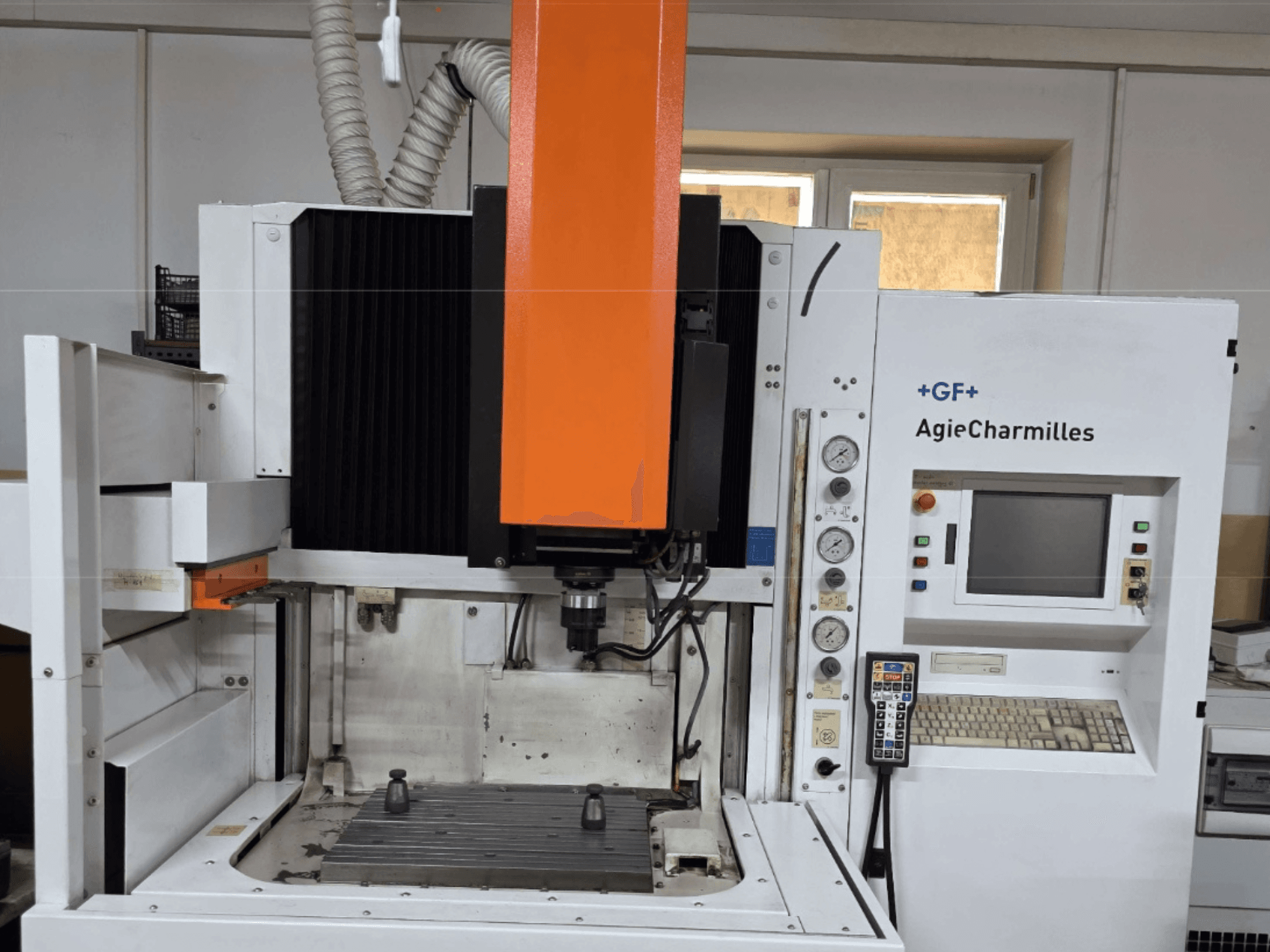 Centro de mecanizado AgieCharmilles en vista frontal con un gran husillo naranja, panel de control y mesa de trabajo visible.