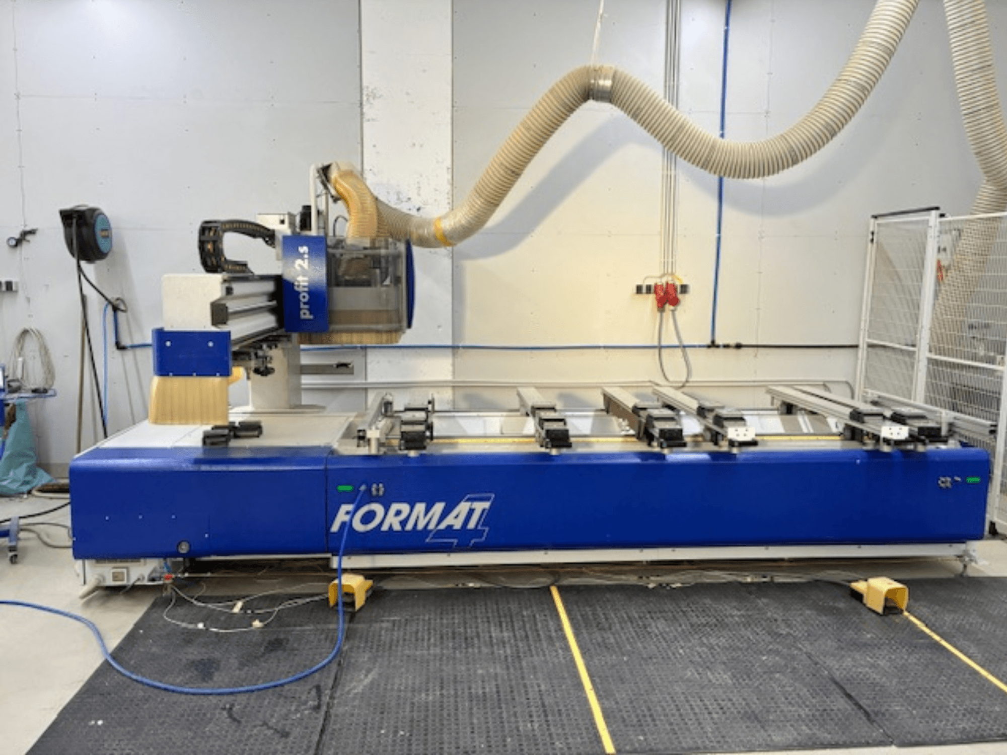 Ruteadora CNC FORMAT 4 azul, modelo Profit 2.5, vista lateral que muestra la zona de corte y el sistema de extracción de polvo, sobre una alfombrilla de goma.