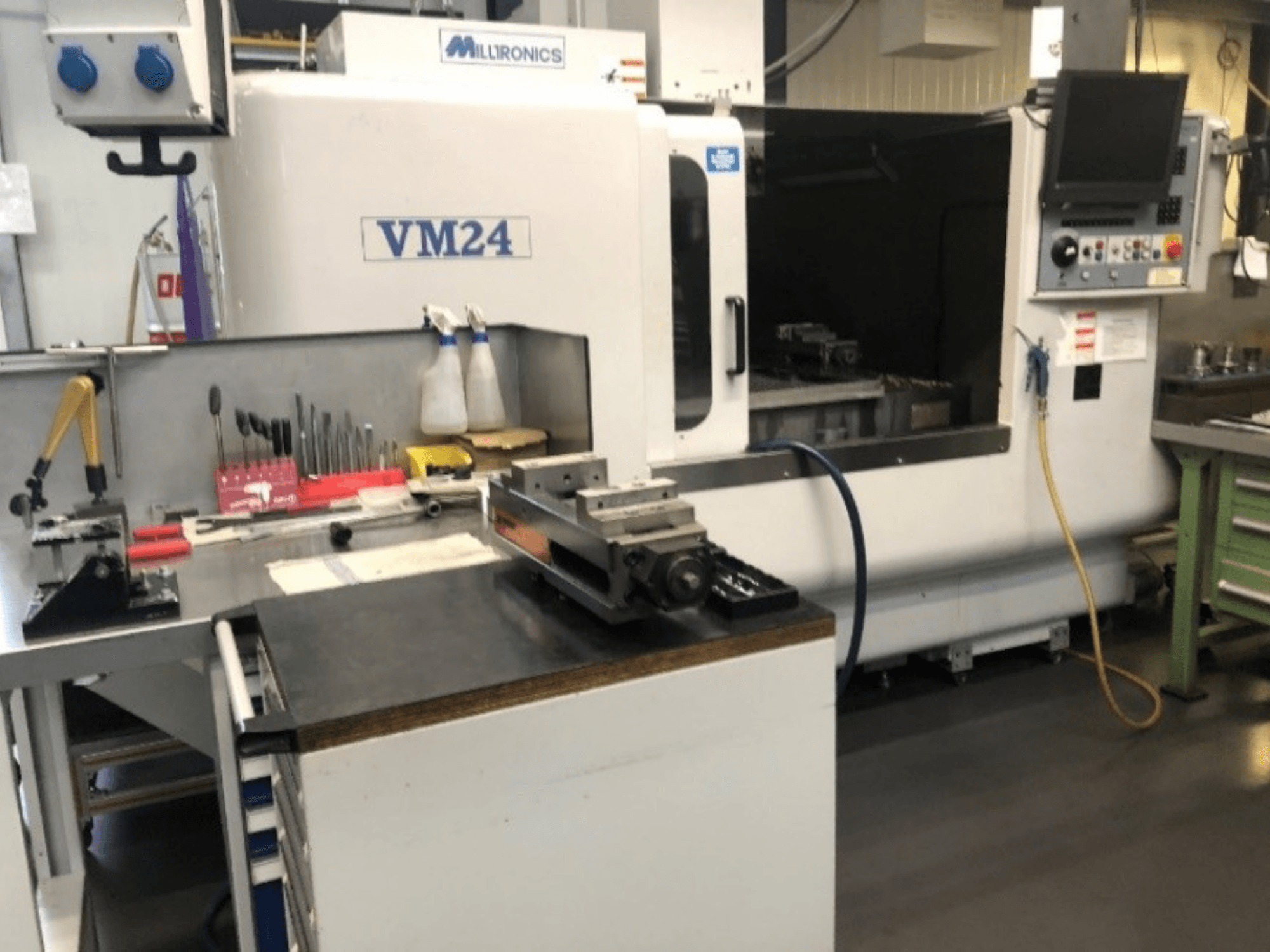 Espacio de trabajo de maquinaria con la máquina CNC Milltronics VM24. Vista frontal con herramientas y equipos en un banco de trabajo.