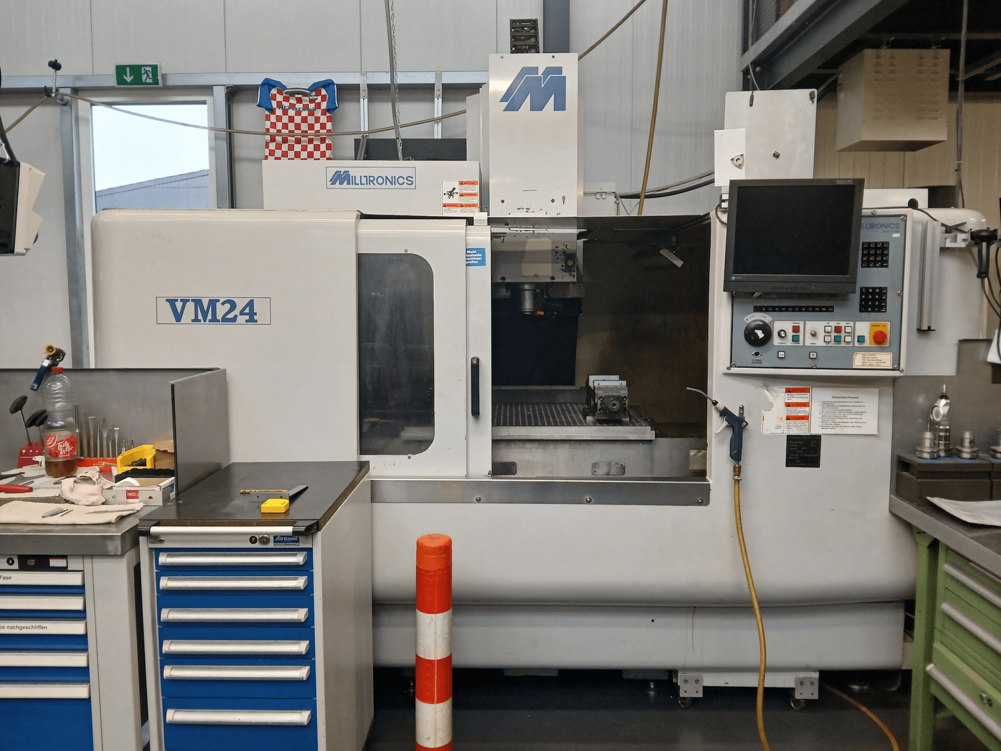 Fresadora CNC Milltronics VM24 mostrada de frente, con panel de control, almacenamiento de herramientas y configuración del área de trabajo.