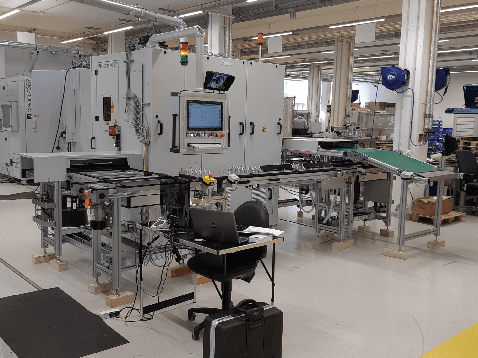 Máquina herramienta CLEAN LASER clean CELL 3220, vista frontal en la que se aprecian el panel de control, la cinta transportadora y la configuración del espacio de trabajo en un entorno industrial.