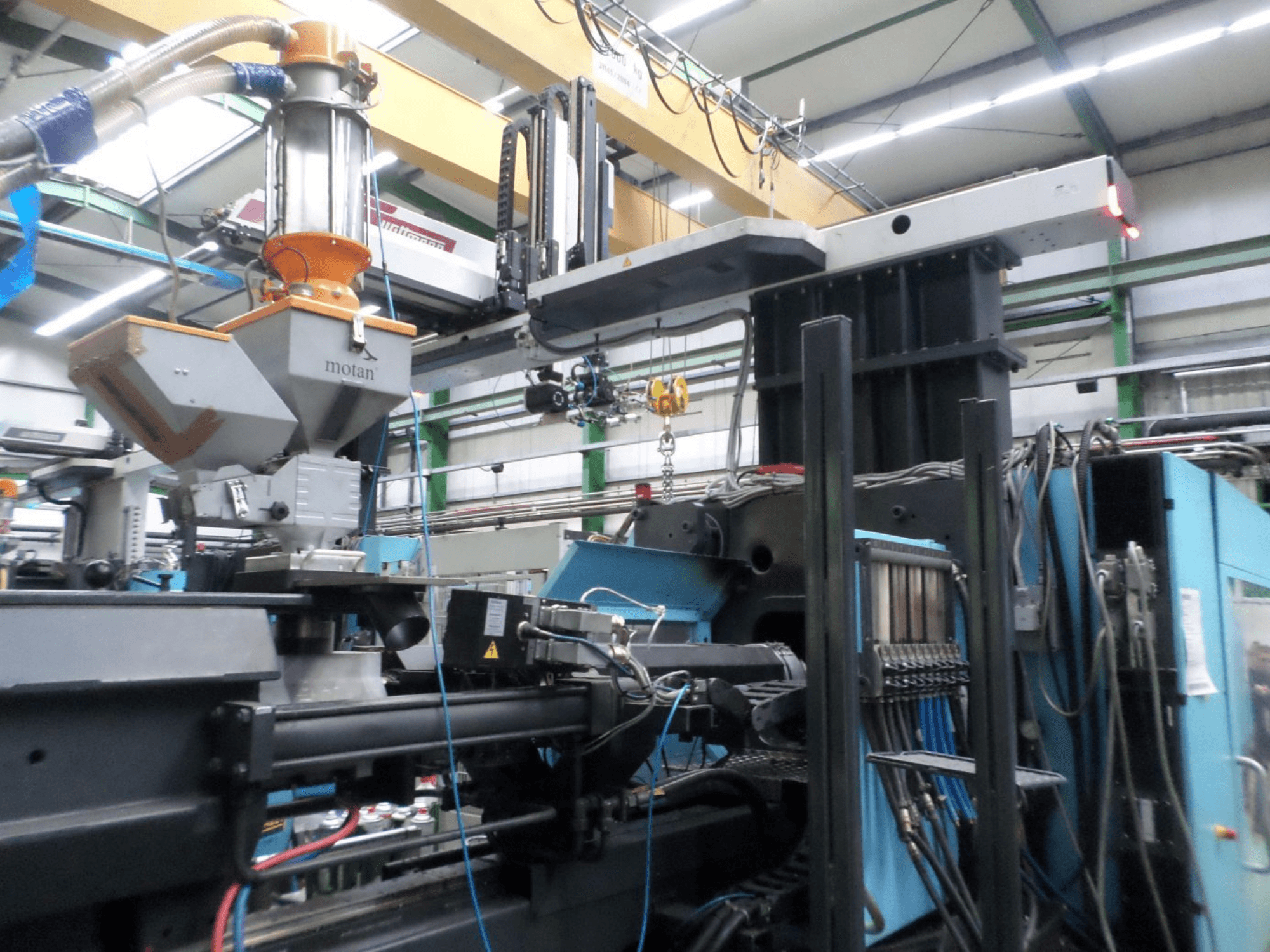 Máquina de moldeo por inyección hidráulica DEMAG D 1300, vista lateral, en la que se aprecian la tolva, la unidad de control y las conexiones en un entorno industrial.
