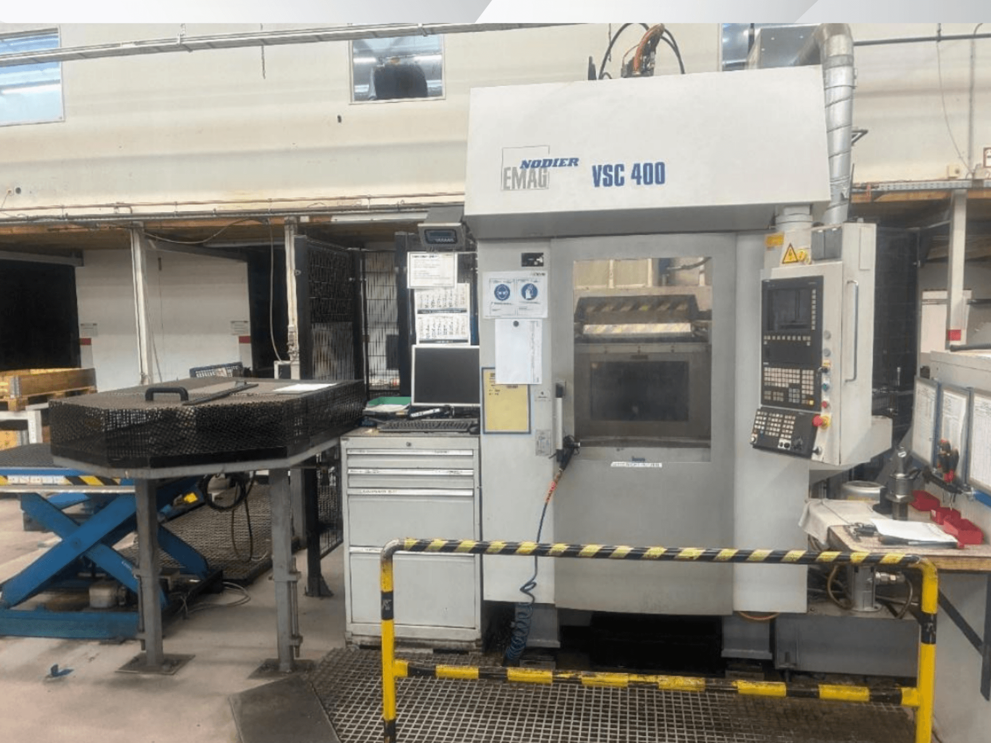 Vista frontal del torno vertical EMAG VSC 400, en la que se aprecian el panel de control, las barreras de seguridad y el equipo circundante en un taller bien iluminado.