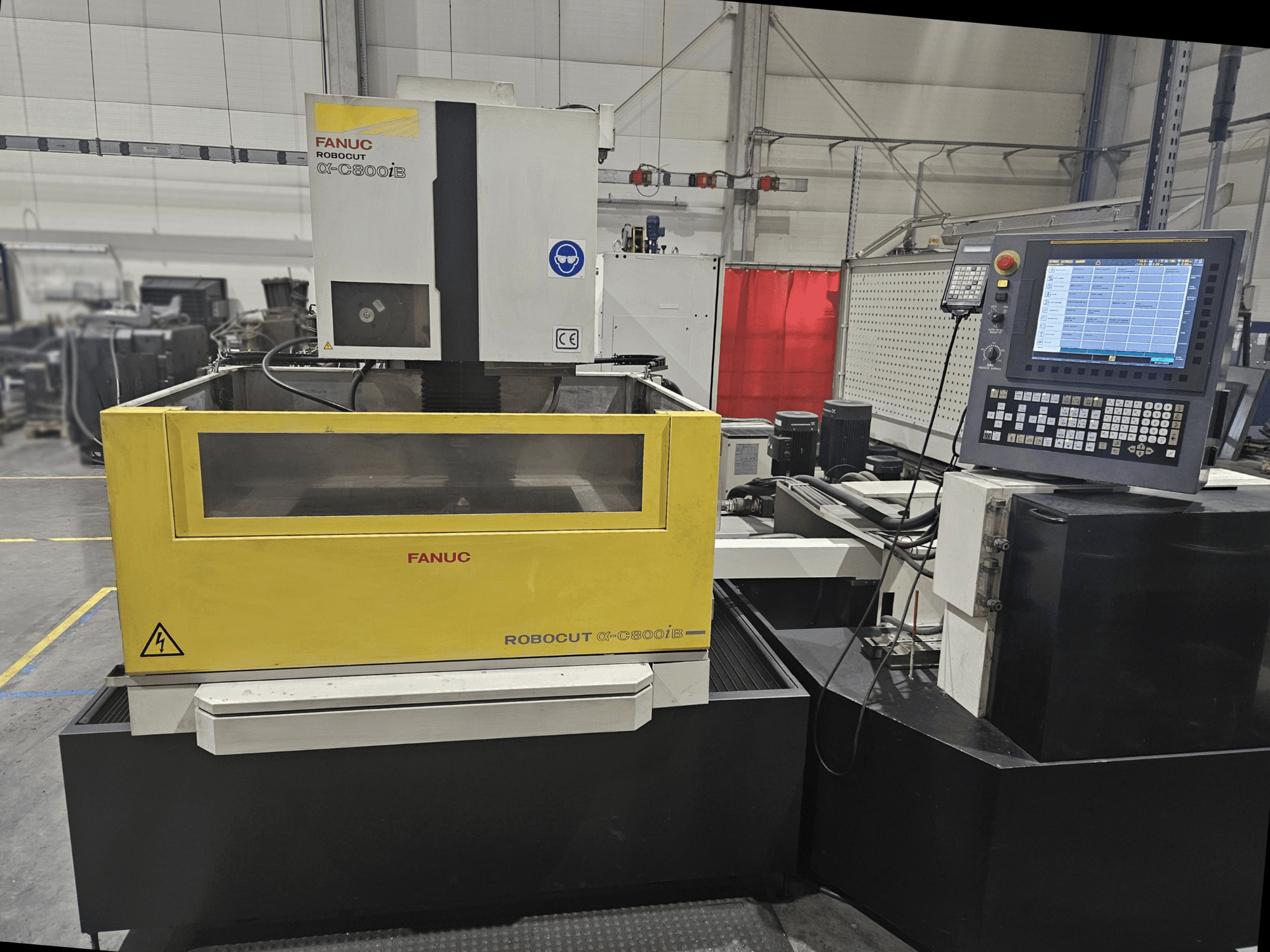 Vista frontal de FANUC Robocut α-C600iB con un cuerpo de máquina amarillo y gris, panel de control CNC y pantalla operativa.