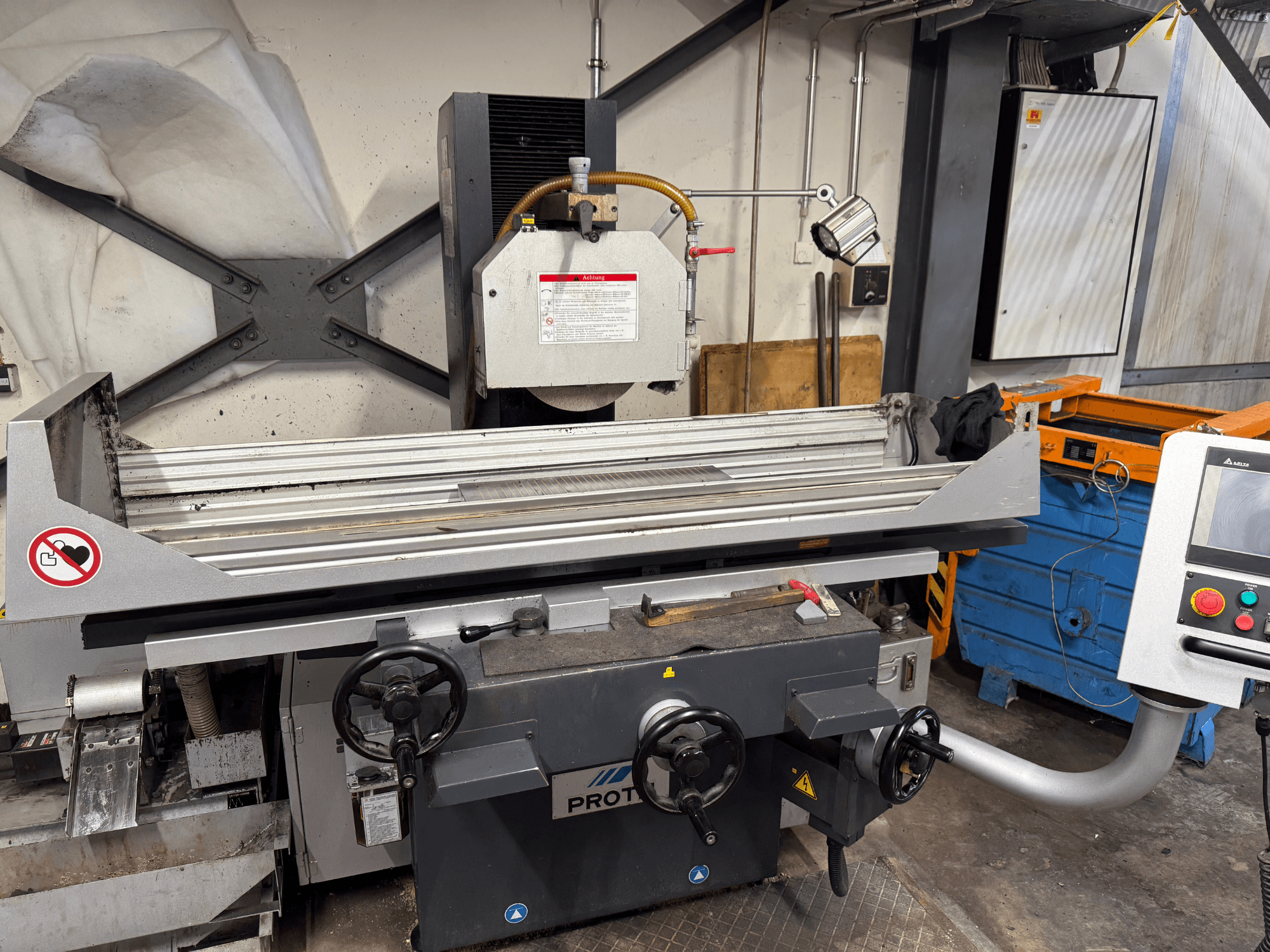 Máquina PROTEC, vista frontal, que muestra una amoladora de superficie con controles manuales, advertencias de seguridad y un sistema de refrigeración.