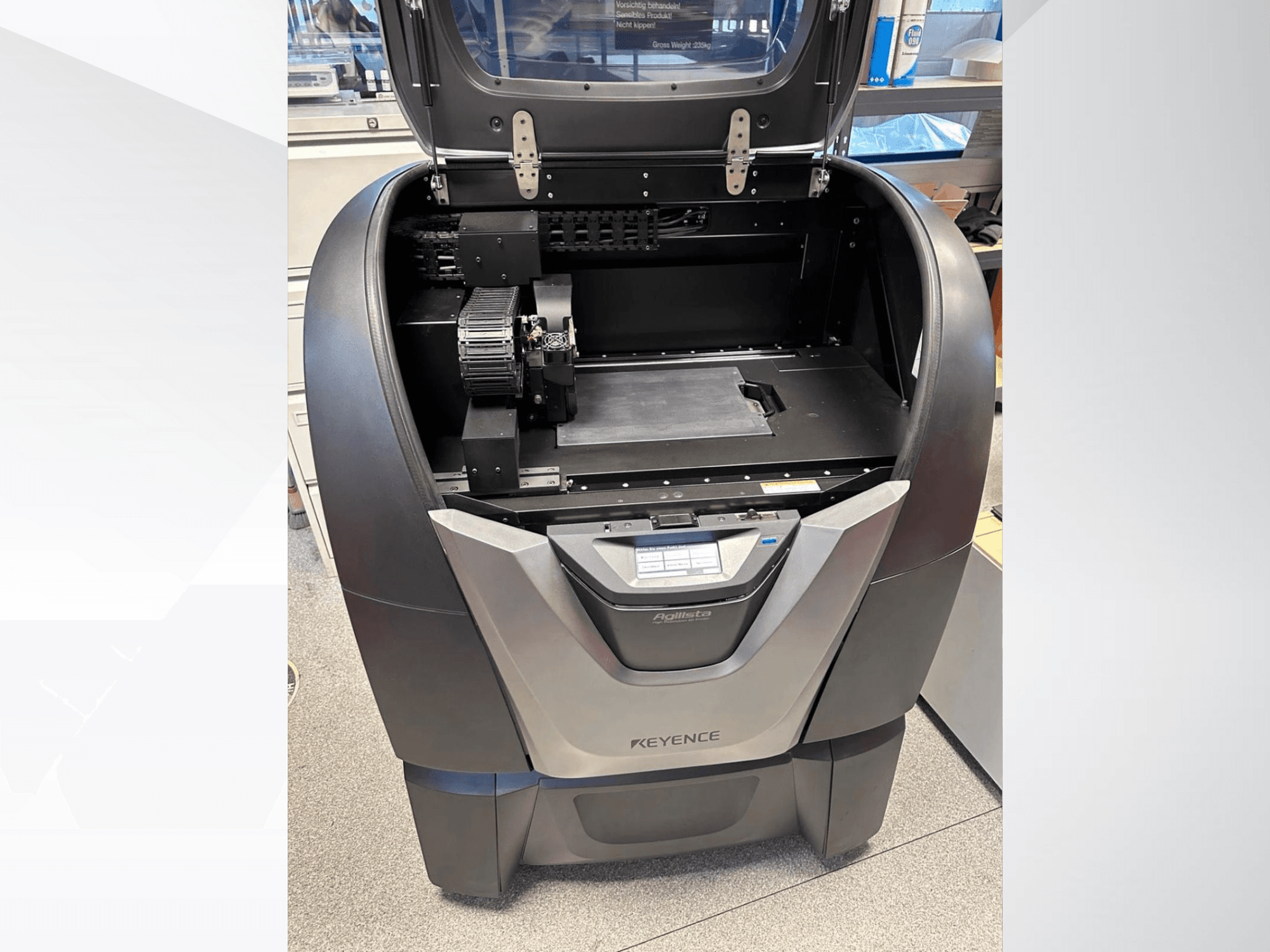 Vista frontal de la impresora 3D KEYENCE Agilista: parte superior abierta, gran plataforma de impresión y componentes mecánicos internos.