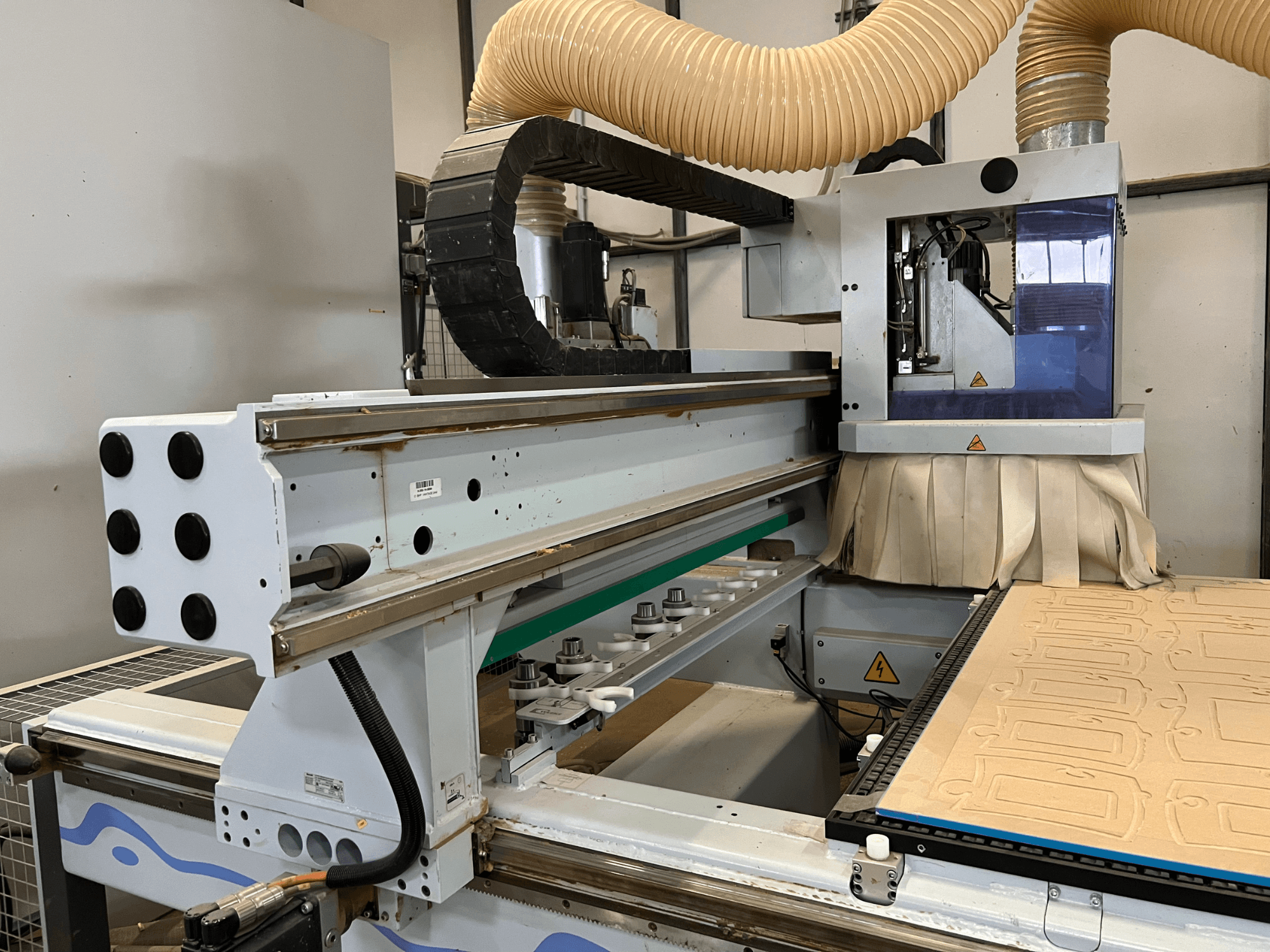 Vista lateral de una fresadora CNC con panel de control azul y plateado, equipada con extracción de polvo y cama de corte de madera.